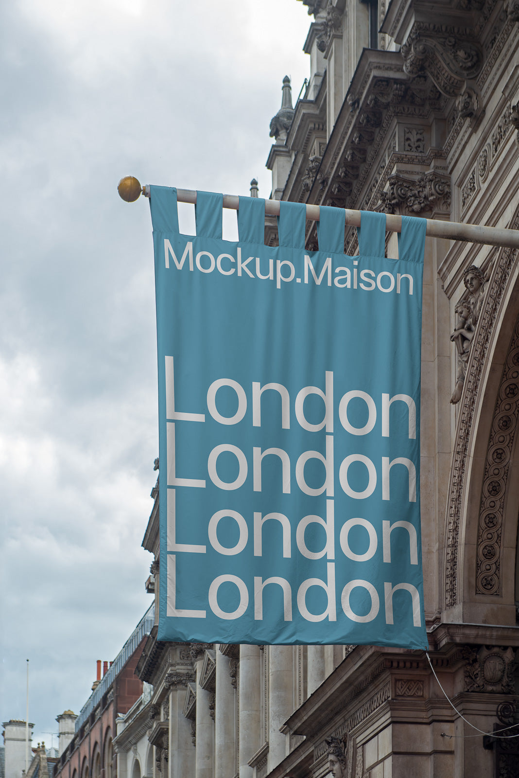 PSD mockup of a blue flag with the text "Mockup.Maison" and multiple "London" words, hanging on a historic building against a cloudy sky.