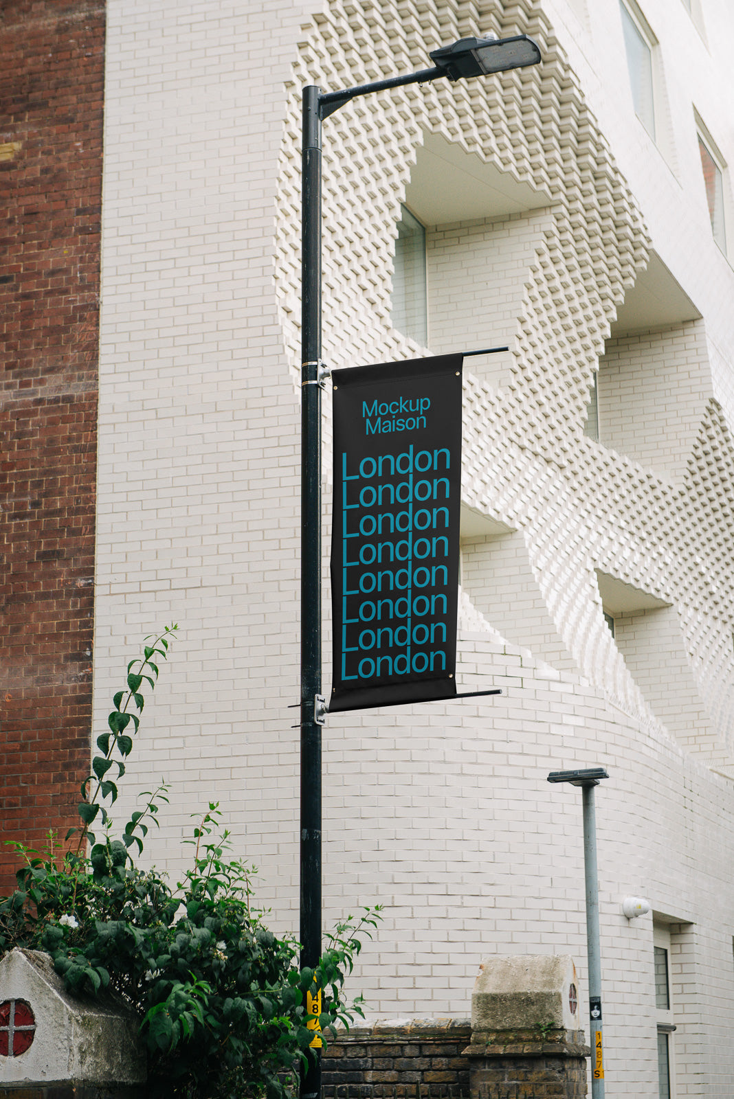 PSD mockup of a vertical street sign mounted on a lamppost in front of a textured white brick building, displaying "London" repeatedly.