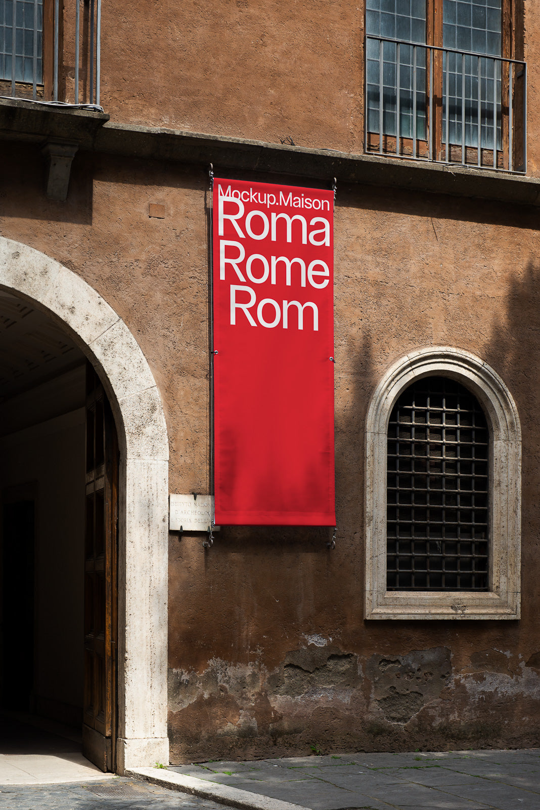 PSD mockup of a red vertical banner hanging on an aged stone building exterior, displaying the word "Rome" in multiple languages.