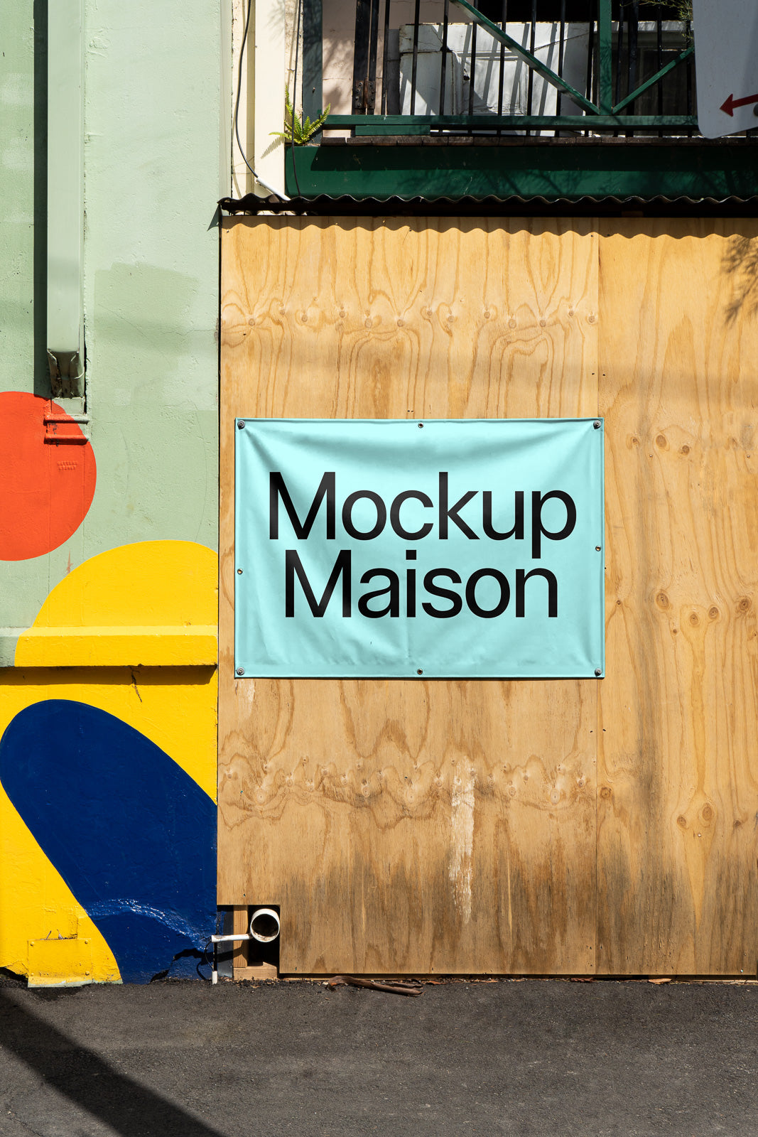 PSD mockup of a light blue banner with "Mockup Maison" text, attached to a wooden wall next to a colorful mural.