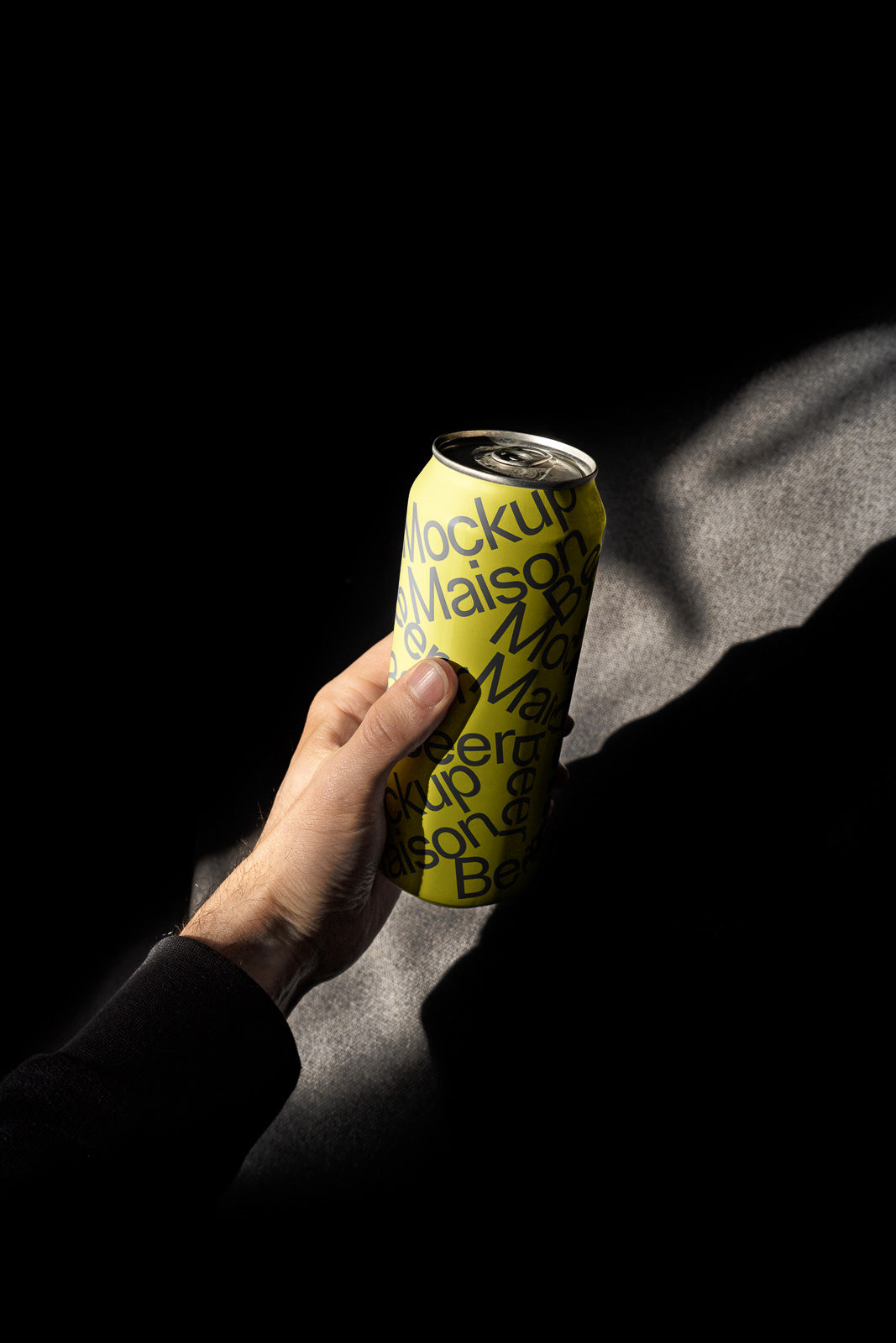 PSD mockup of a person holding a yellow beverage can with bold black text against a dark background, showcasing design details and shadows.