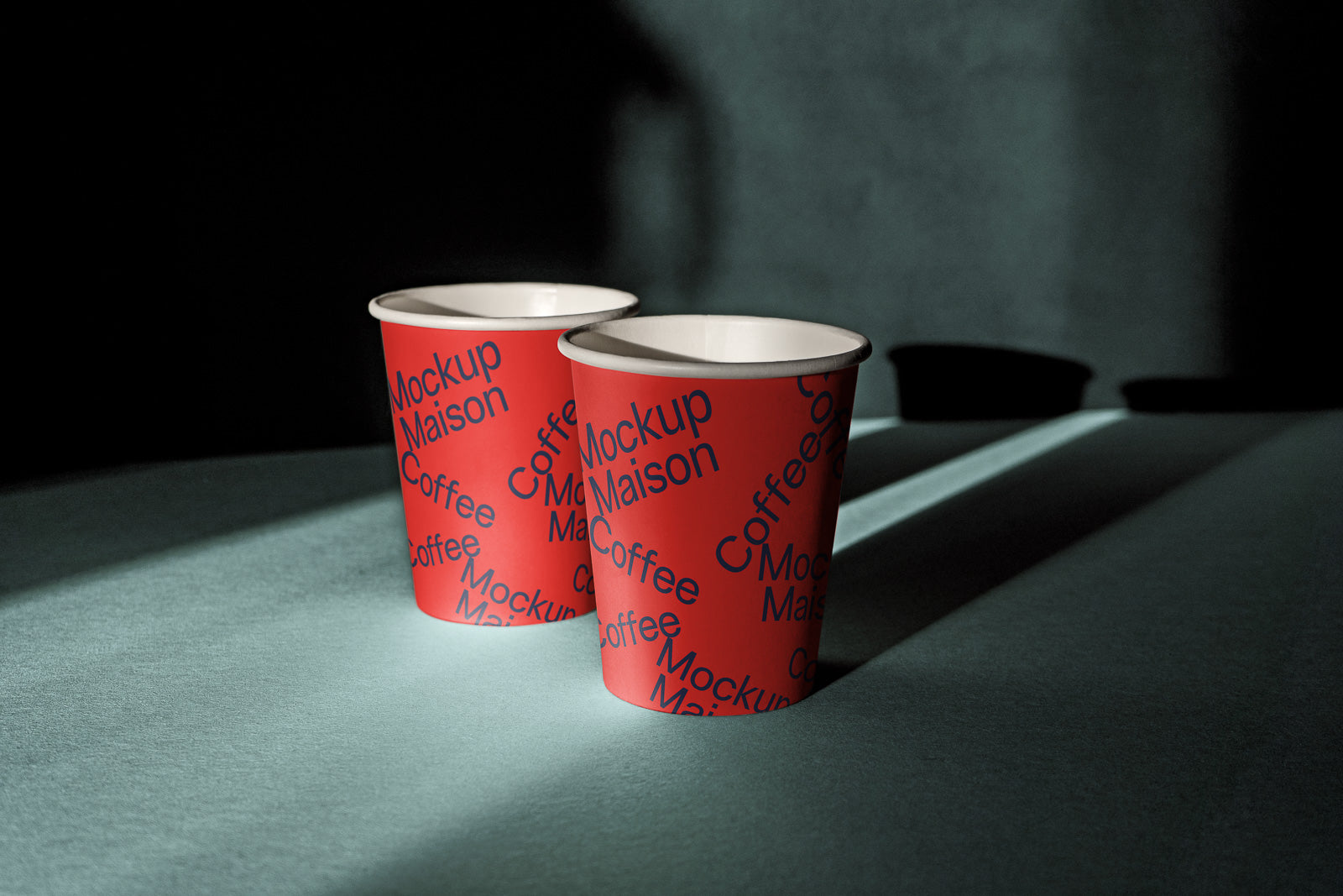 PSD mockup of two red paper coffee cups with blue text, placed on a light blue surface with dramatic shadows and a dark background.