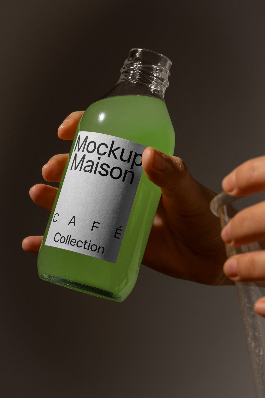 PSD mockup of a green beverage bottle labeled "Mockup Maison Café Collection," held by a hand against a soft background.