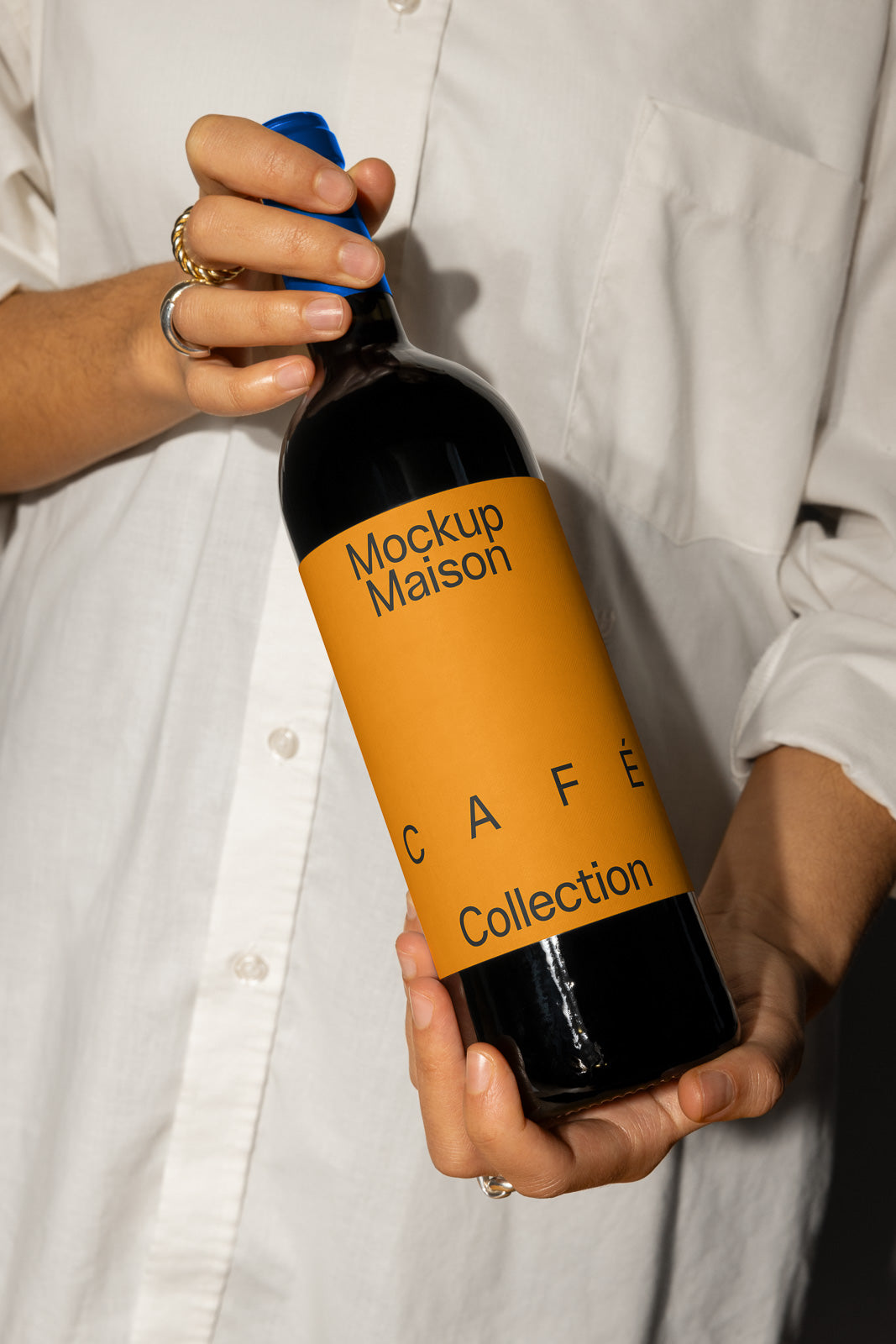 PSD mockup of a wine bottle with an orange label titled "Mockup Maison Café Collection," held by a person wearing a white shirt.