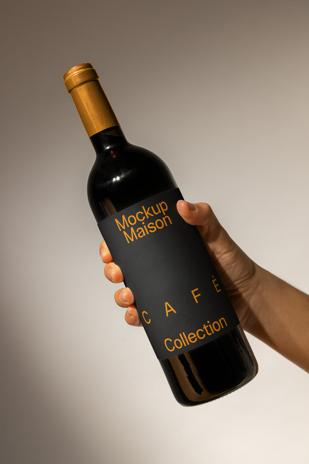 PSD mockup of a wine bottle with a black label featuring the text "Mockup Maison CAFE Collection," held by a hand against a neutral background.