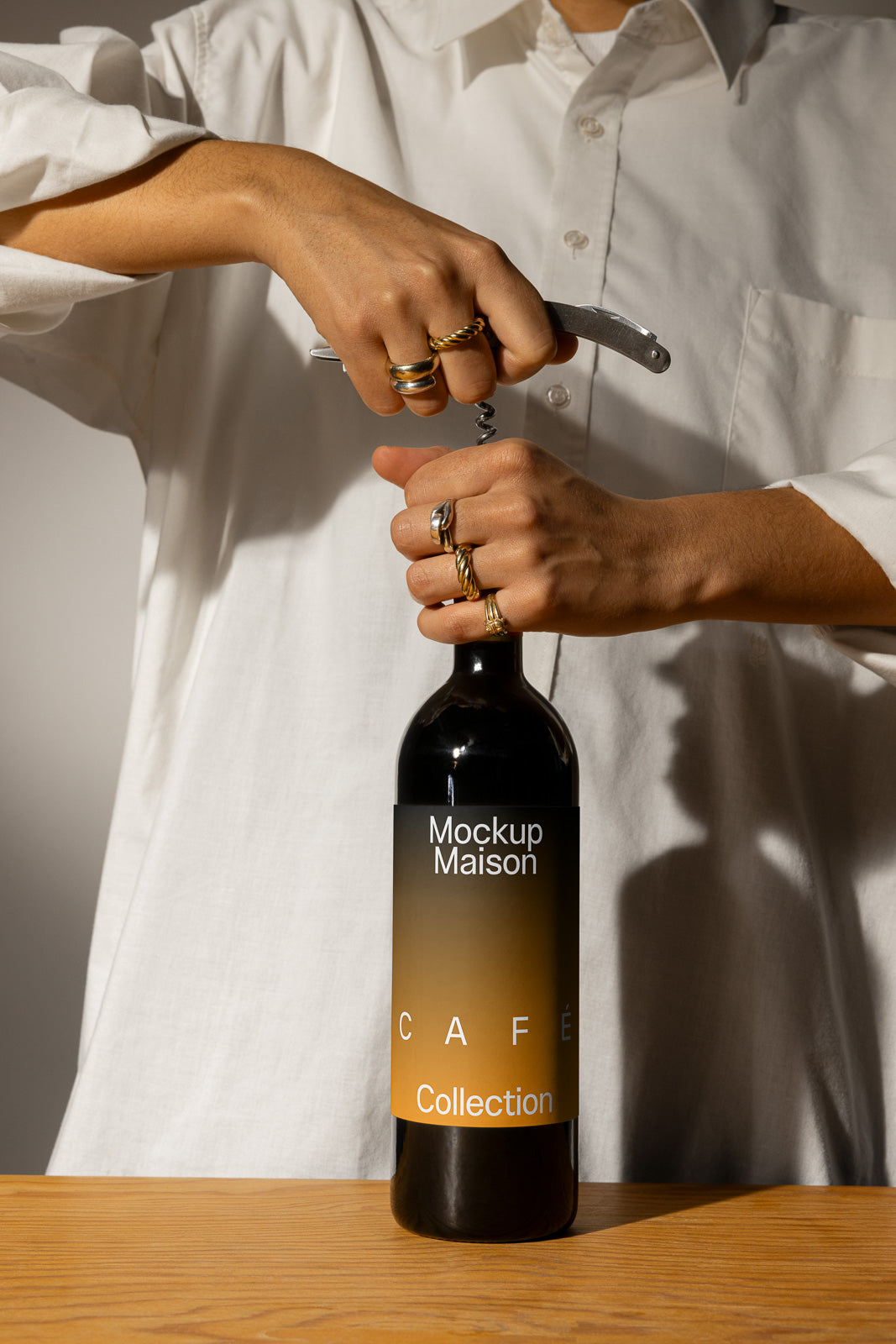 PSD mockup of a person in a white shirt opening a wine bottle labeled "Mockup Maison Café Collection" with a corkscrew.