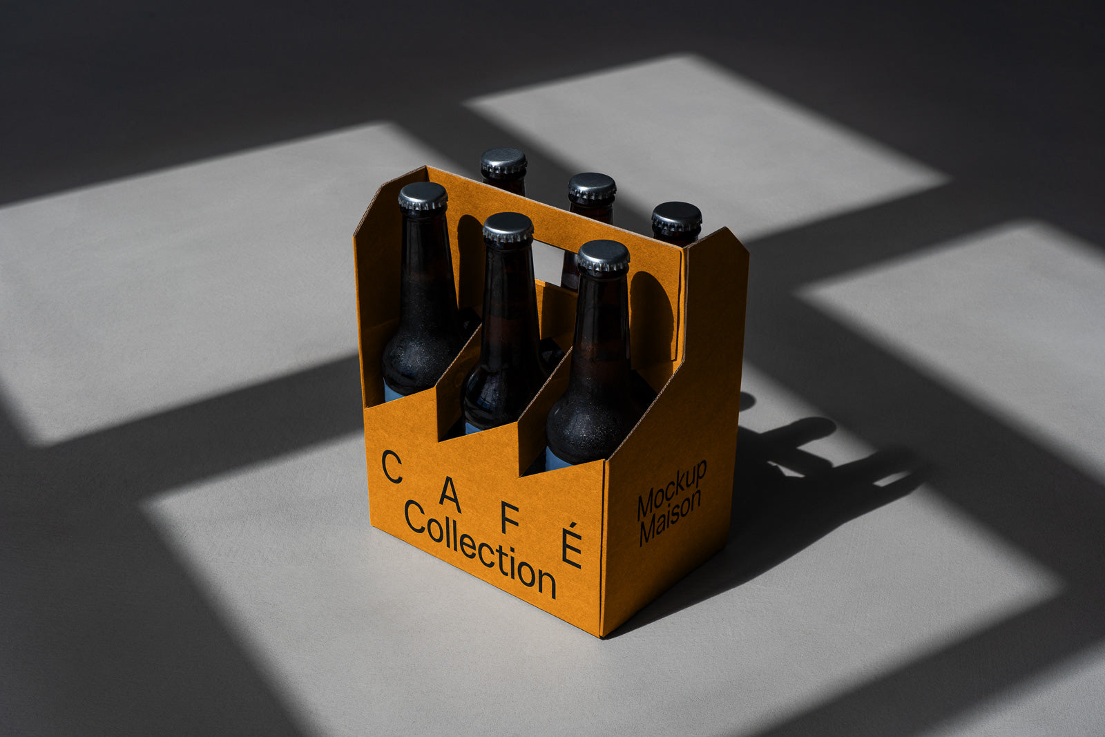 PSD mockup of a cardboard carrier holding six dark glass bottles, labeled "Café Collection" and "Mockup Maison," casting shadows on a gray surface.