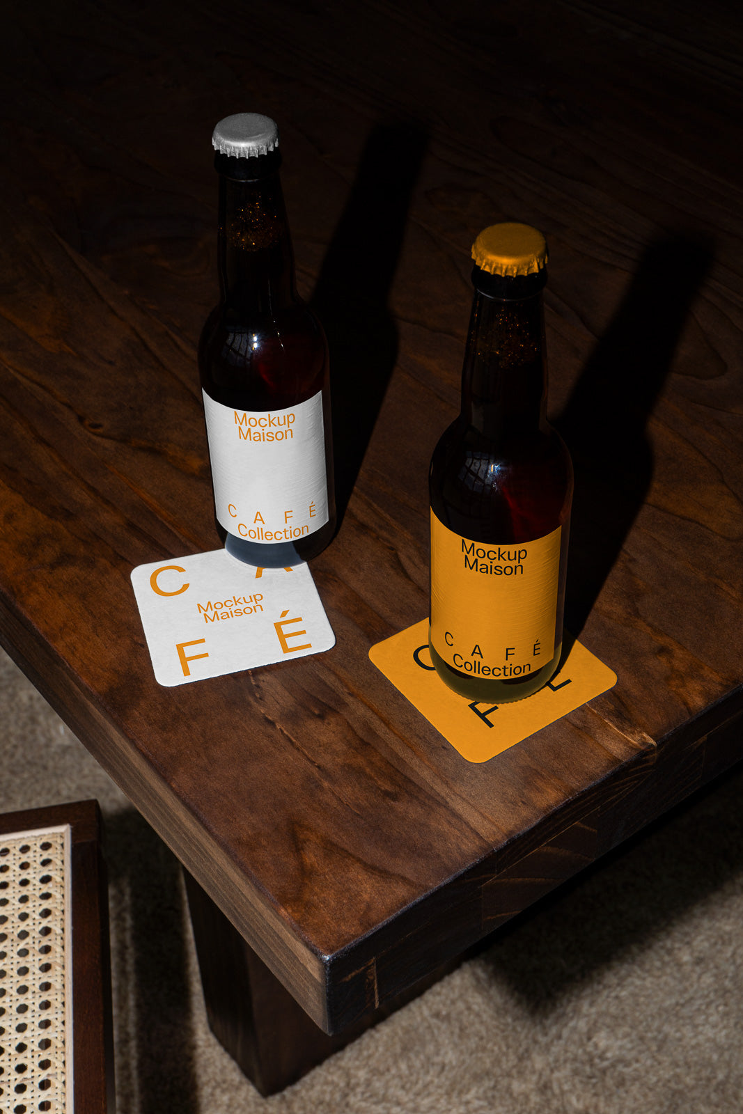 PSD mockup of two beer bottles labeled "Mockup Maison Café Collection" on a wooden table, each placed on a coaster matching their label design.