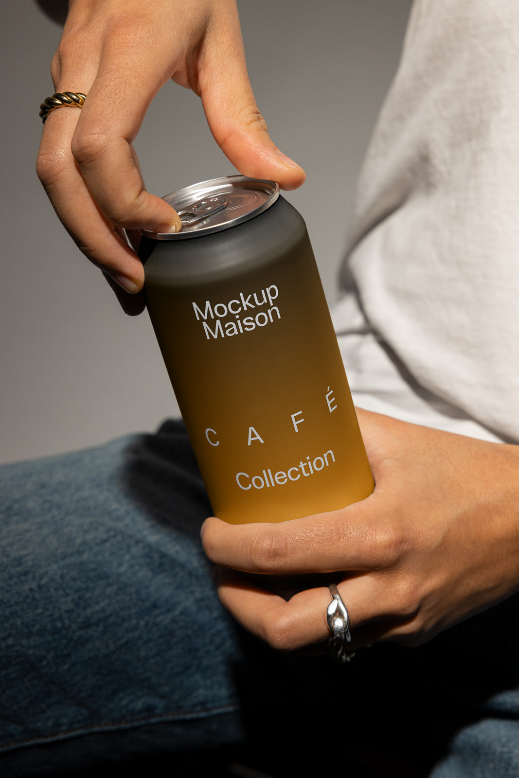 PSD mockup of a hand holding a can labeled "Mockup Maison CAFE Collection," showing a close-up of fingers ready to open the can.
