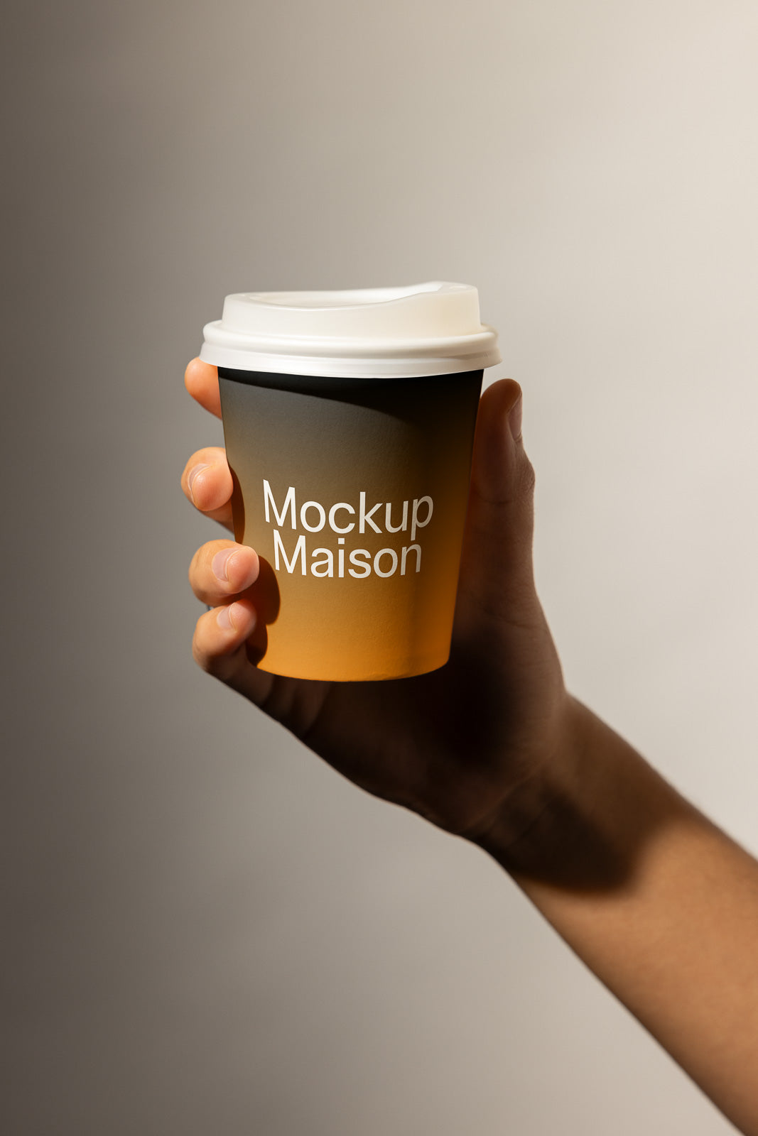 PSD mockup of a hand holding a small coffee cup with "Mockup Maison" printed on a gradient orange to black background, under soft lighting.