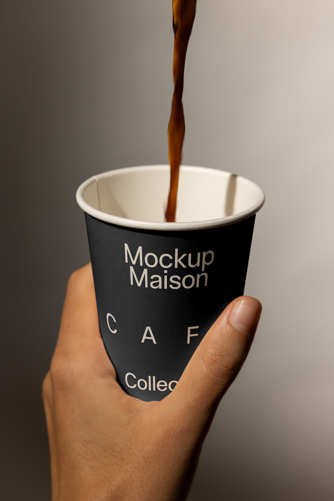 PSD mockup of a hand holding a black paper cup labeled "Mockup Maison" with a liquid being poured in.