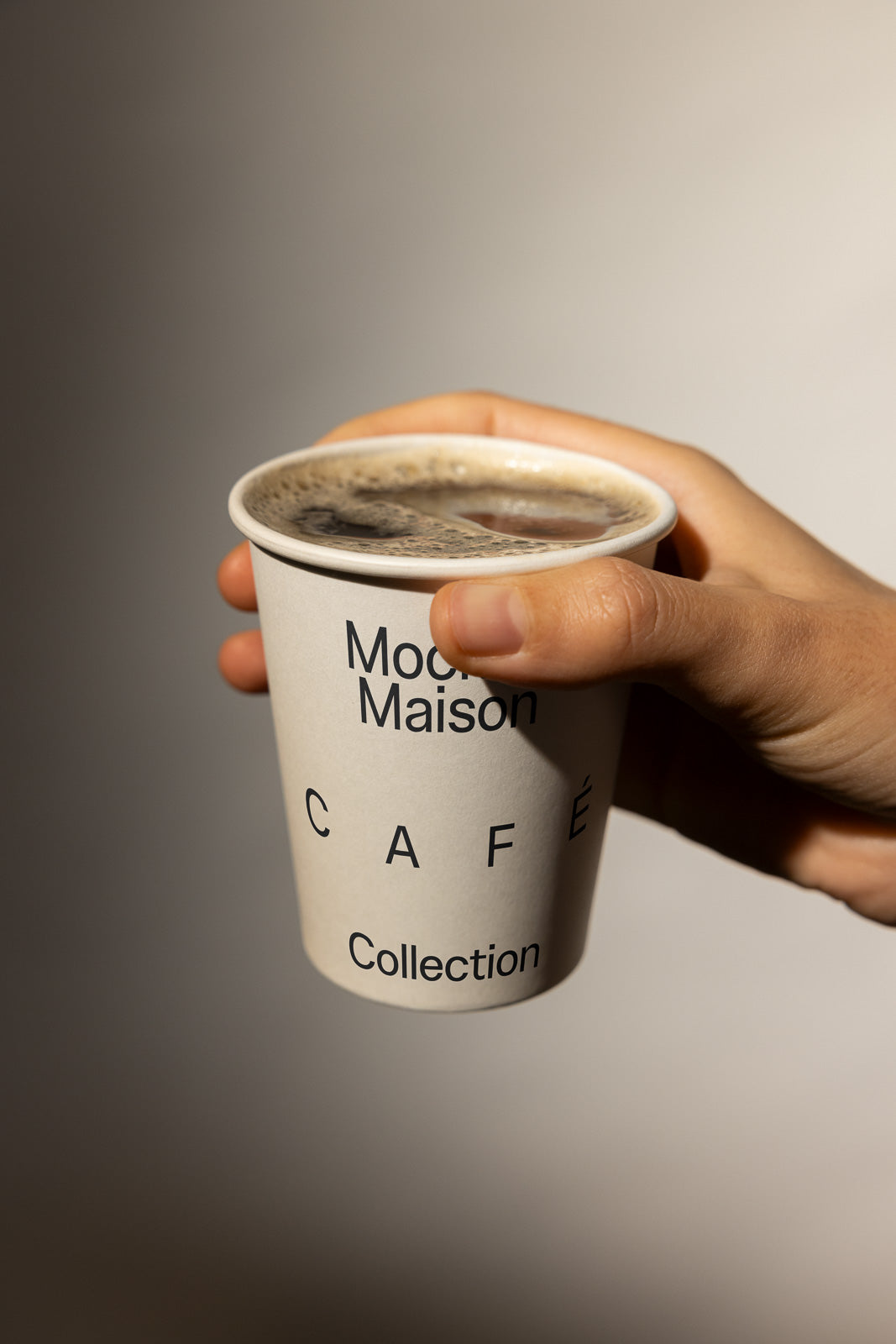 PSD mockup of a hand holding a coffee cup with text "Modern Maison Café Collection," highlighting the sleek design against a neutral background.