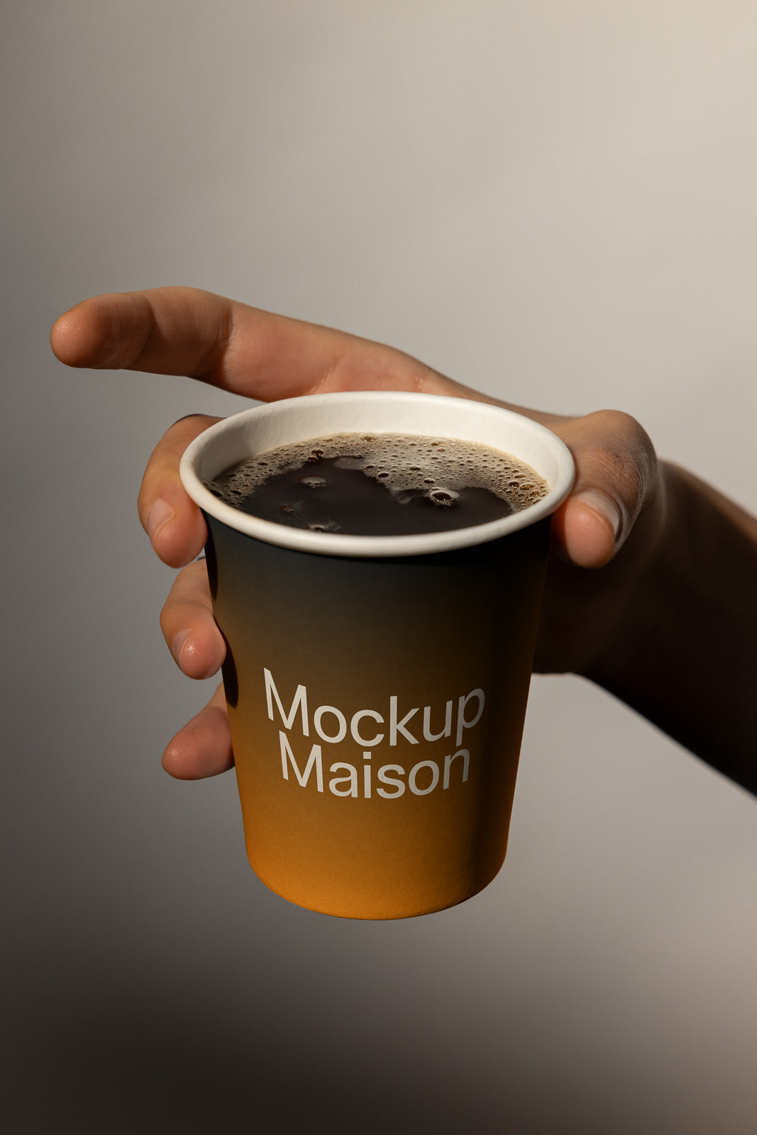 PSD mockup of a hand holding a paper cup filled with coffee, labeled "Mockup Maison," against a neutral background.