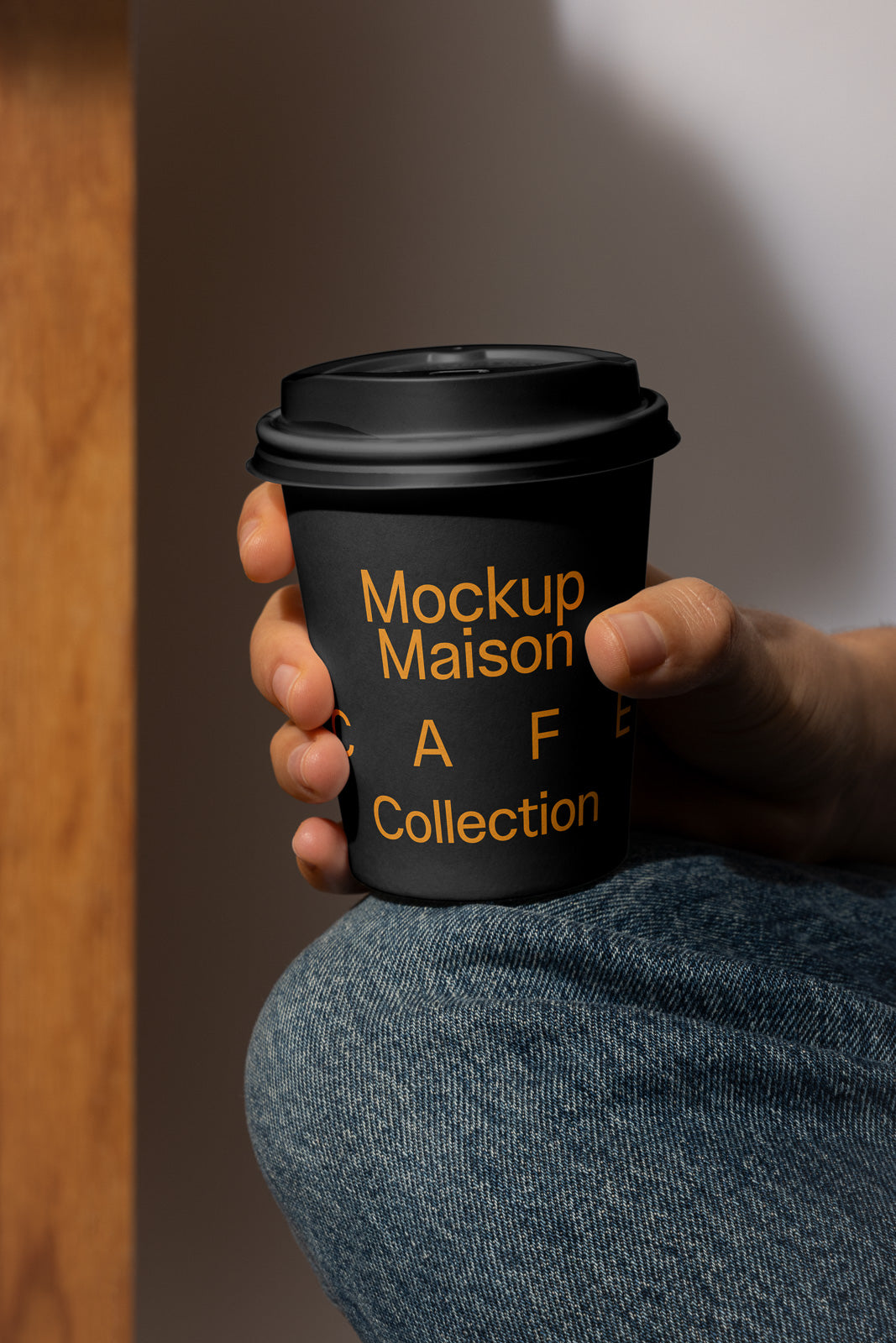 PSD mockup of a black coffee cup with yellow text, held by a hand, against a simple background.