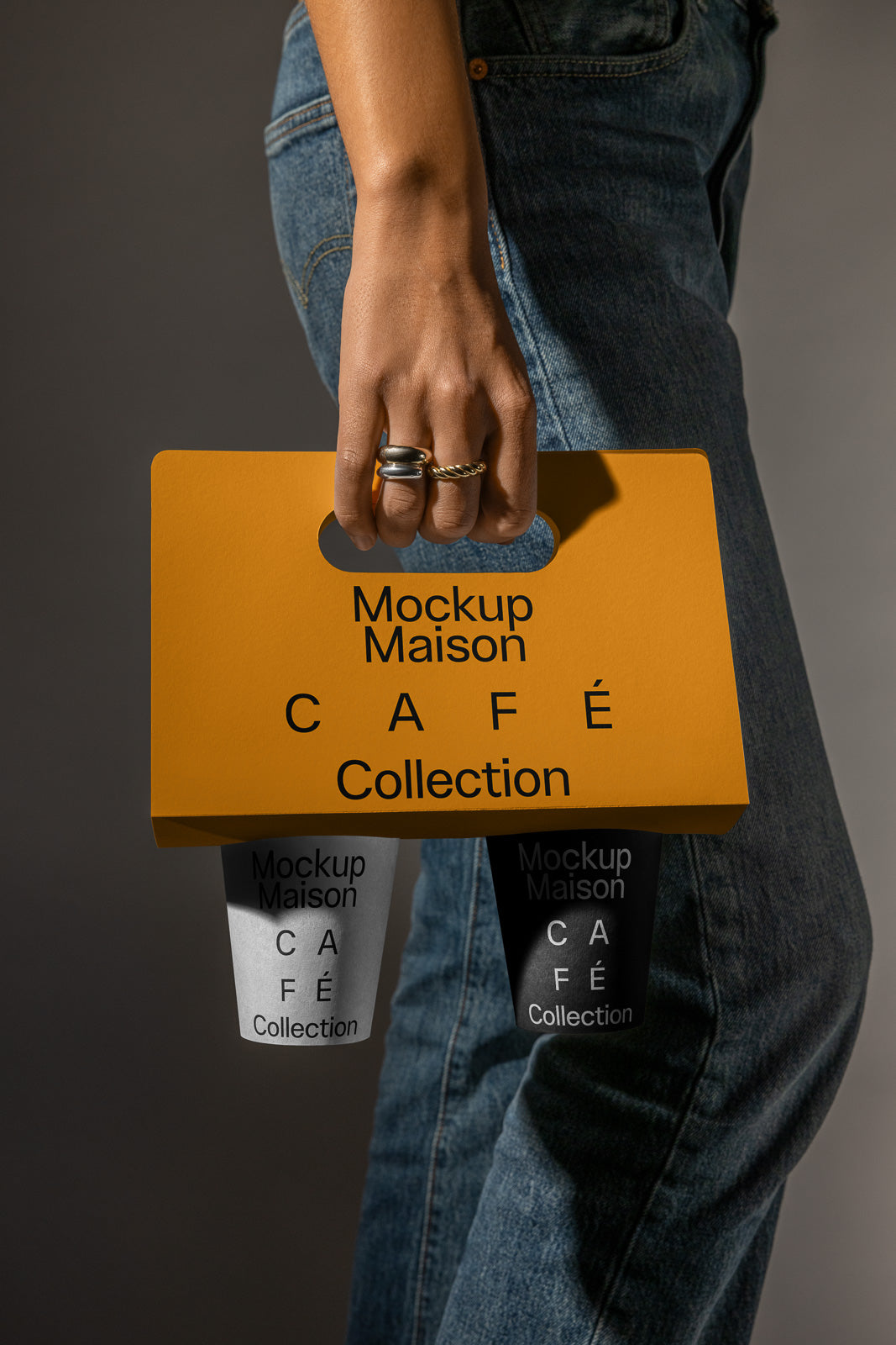 PSD mockup of a person holding a cardboard coffee cup holder with "Mockup Maison Café Collection" printed on it, and two cups inside.