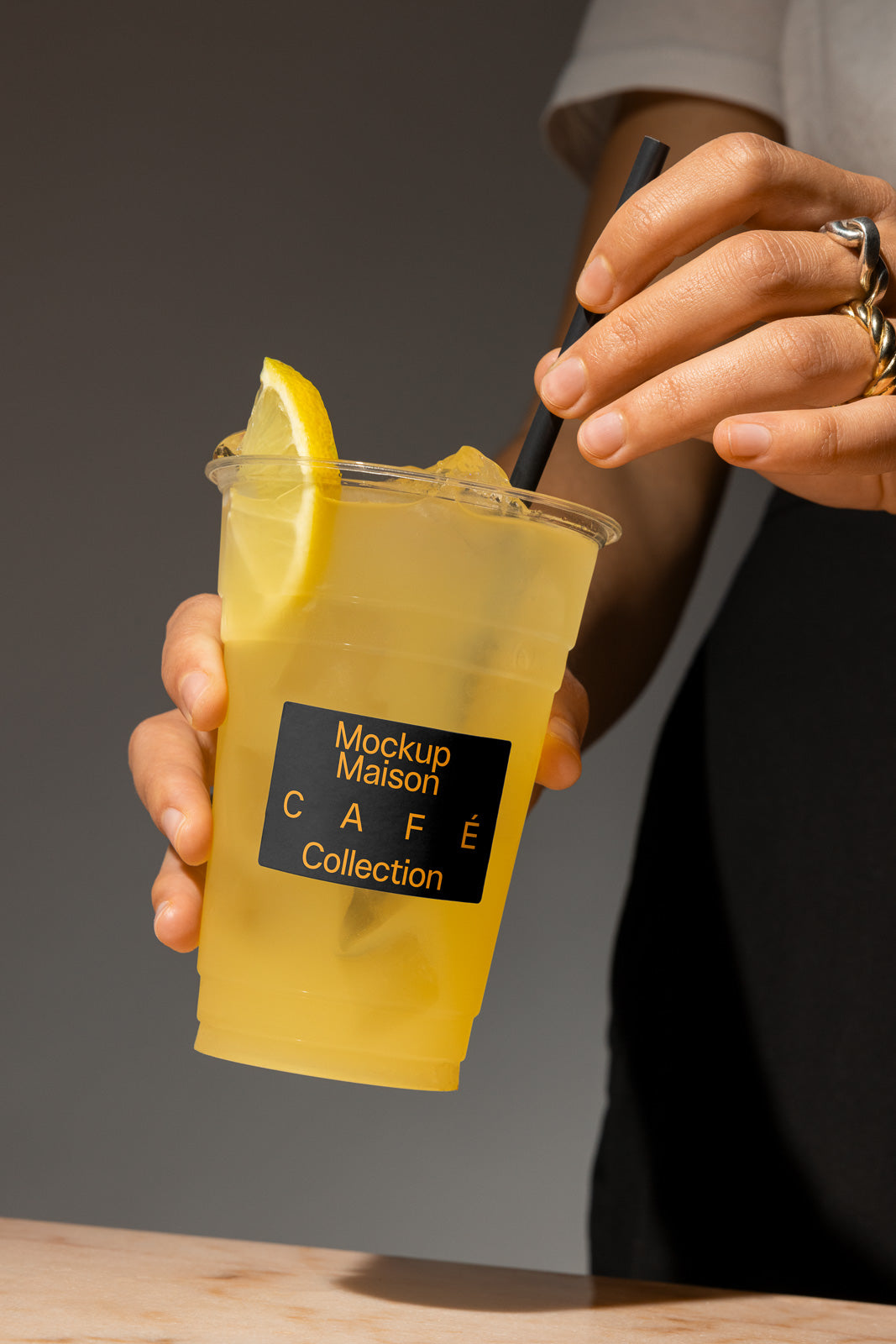 PSD mockup of a hand holding a plastic cup with lemonade, ice, and a lemon slice, featuring the label "Mockup Maison Café Collection."