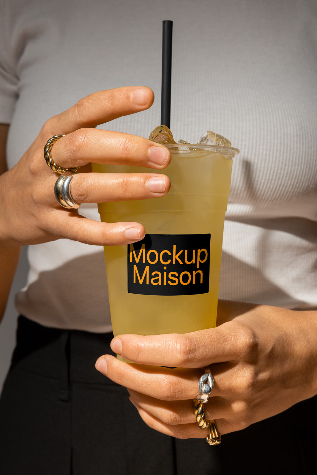 PSD mockup of a person holding a clear cup with ice and a yellow beverage, featuring a black straw and "Mockup Maison" label.