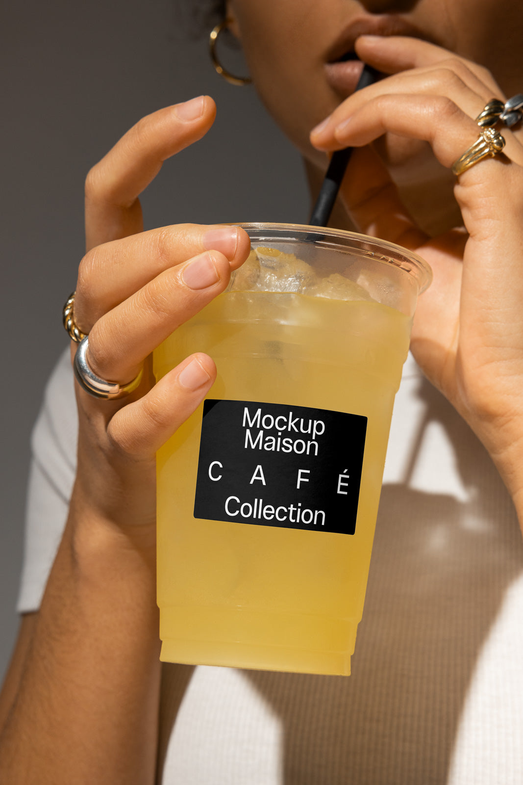 PSD mockup of a person holding a clear cup with a black straw, featuring a café collection label, filled with a yellow drink against a neutral background.