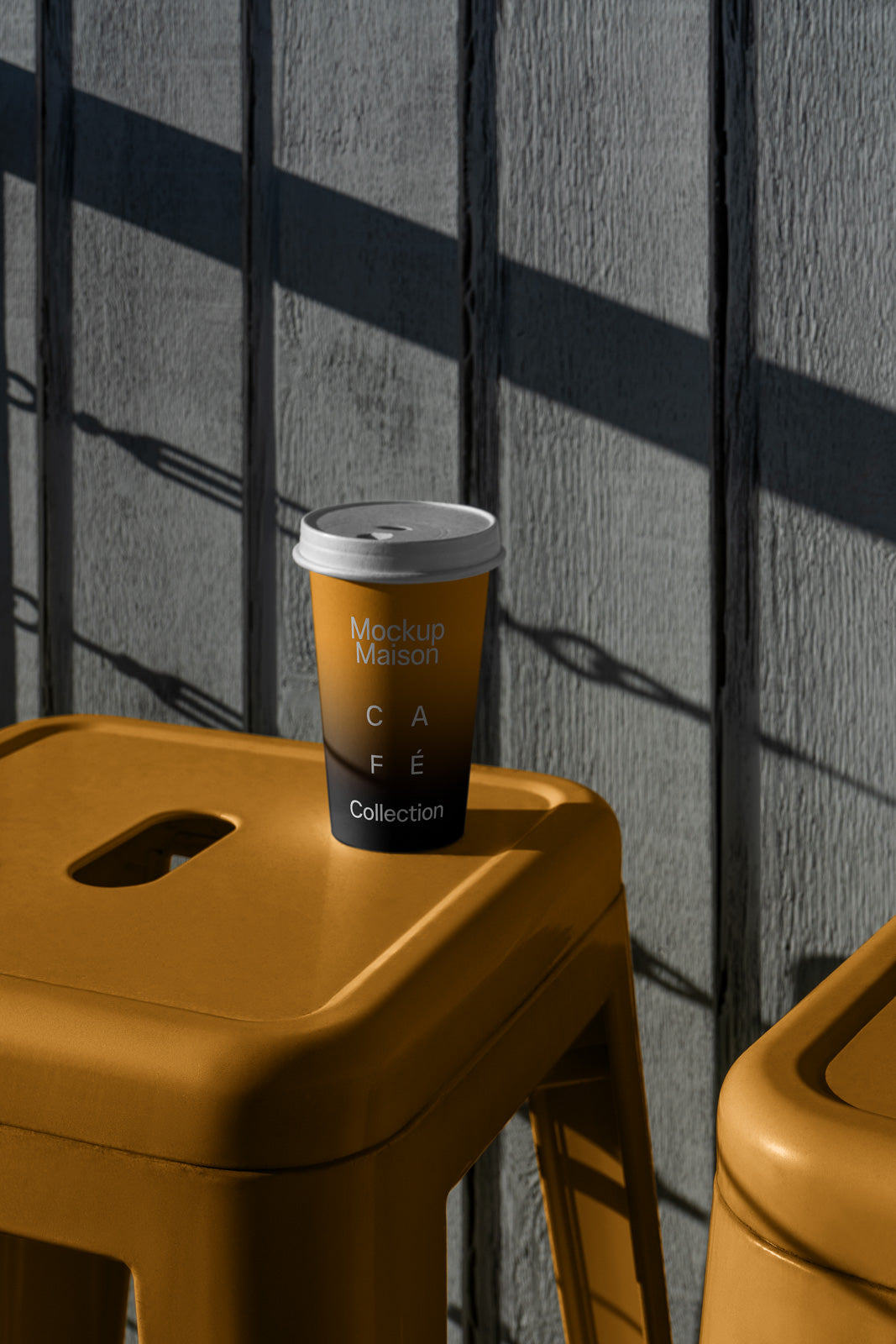 PSD mockup of a branded coffee cup on a yellow chair, casting shadows on a textured gray wall, highlighting minimalist design elements.