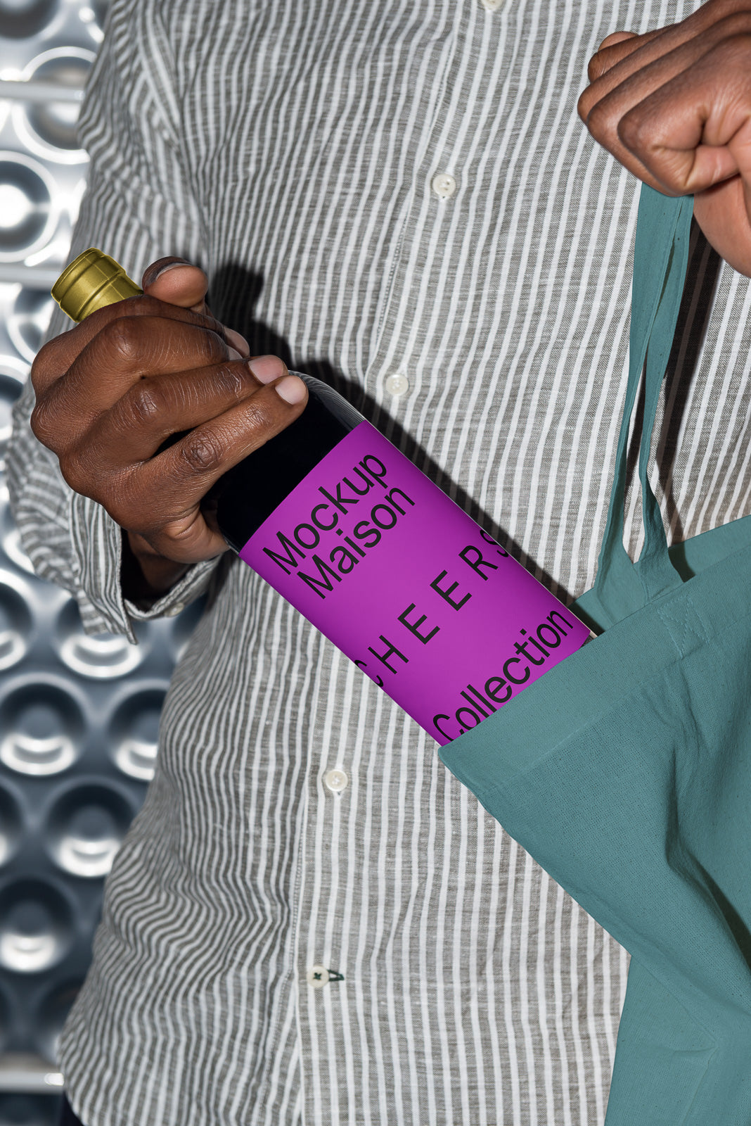 PSD mockup of a wine bottle with a magenta label reading "Mockup Maison CHEERS Collection," held partially inside a green tote bag.