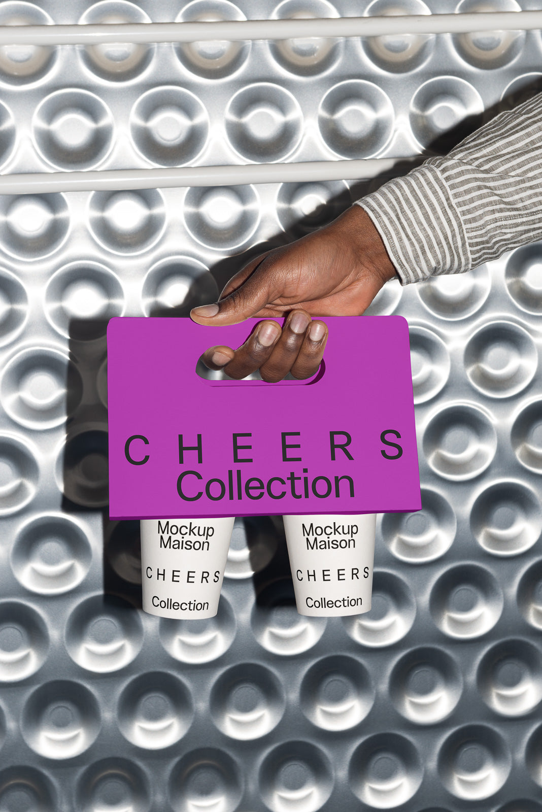 PSD mockup of a hand holding a purple Cheers Collection carrier with two beverage cups, against a bubble-patterned metallic background.