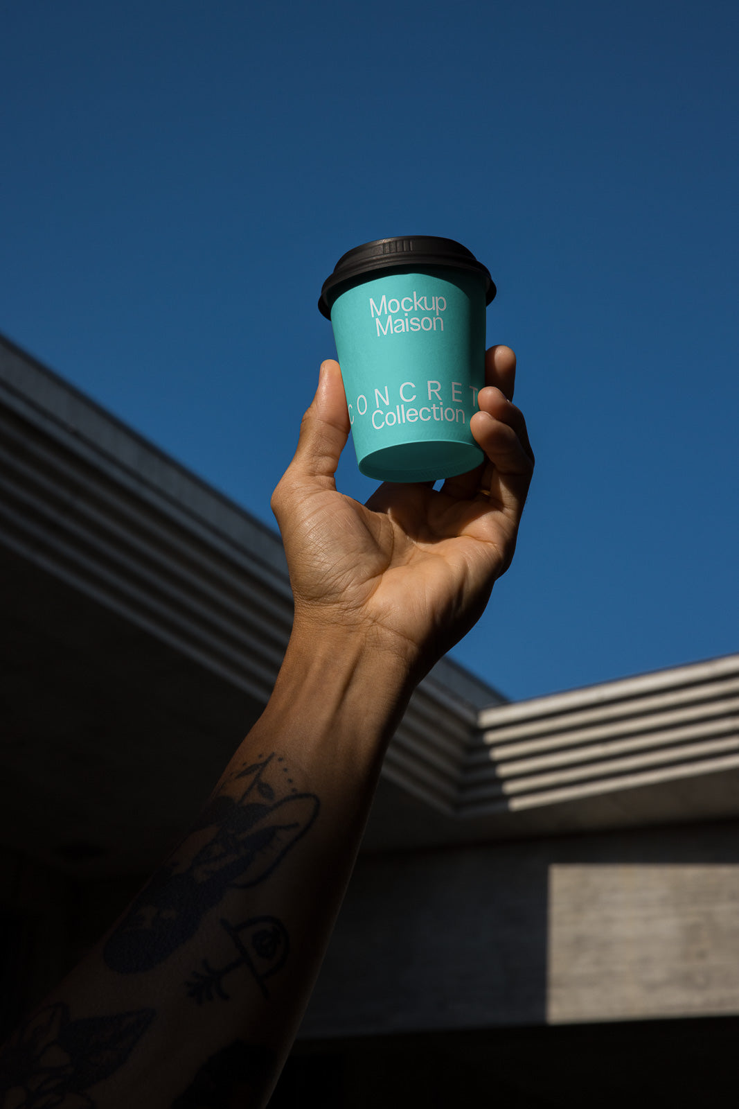 PSD mockup of a hand holding a blue coffee cup with "Mockup Maison" and "Concrete Collection" text, set against a clear blue sky background.