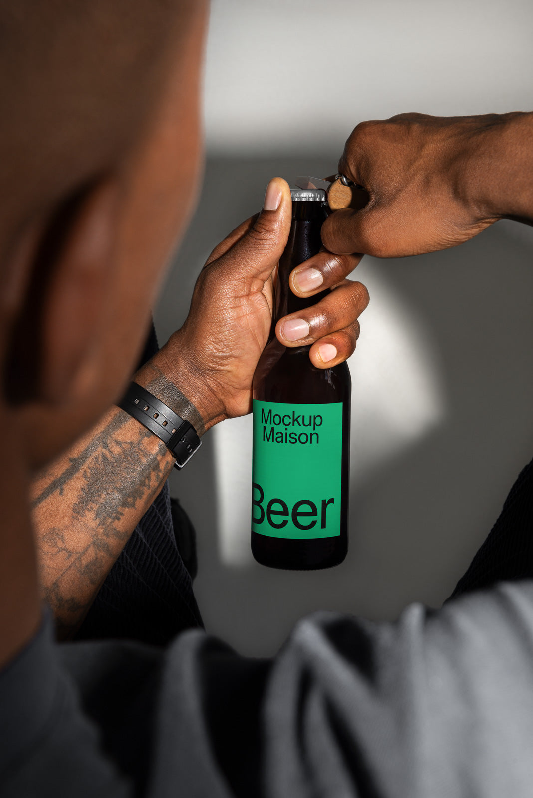 PSD mockup of a beer bottle with a green label being opened by a person using a bottle opener, highlighting product design details.