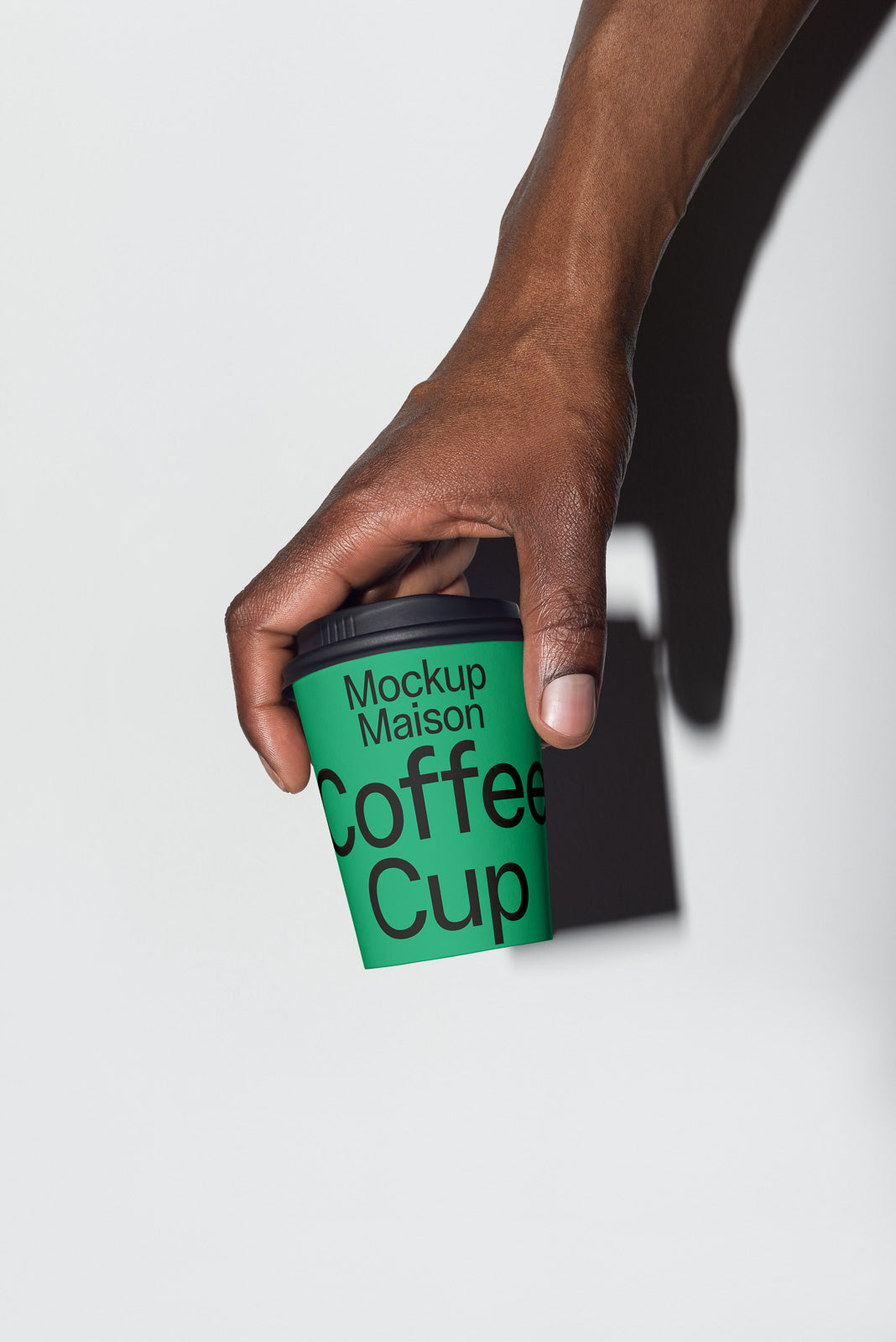 PSD mockup of a hand holding a green coffee cup labeled "Mockup Maison Coffee Cup" against a light background, casting a shadow.