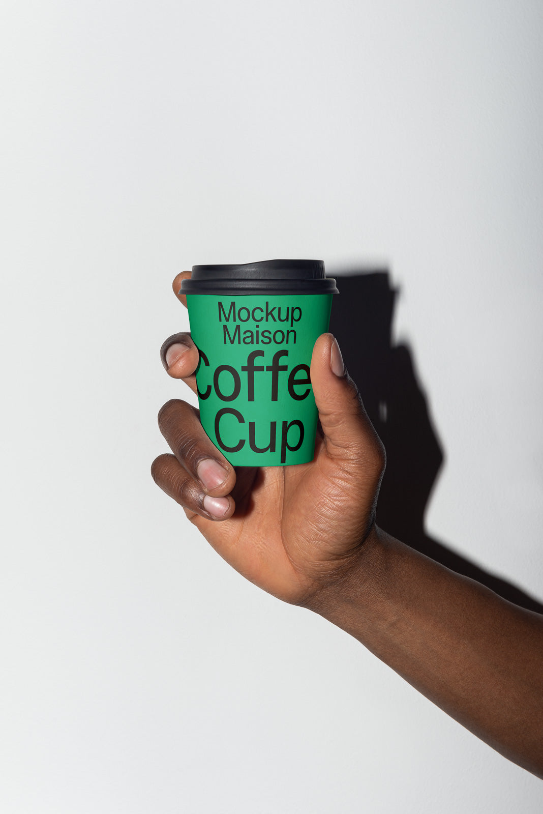 PSD mockup of a green coffee cup with black text held in a hand, casting a shadow on a light background.
