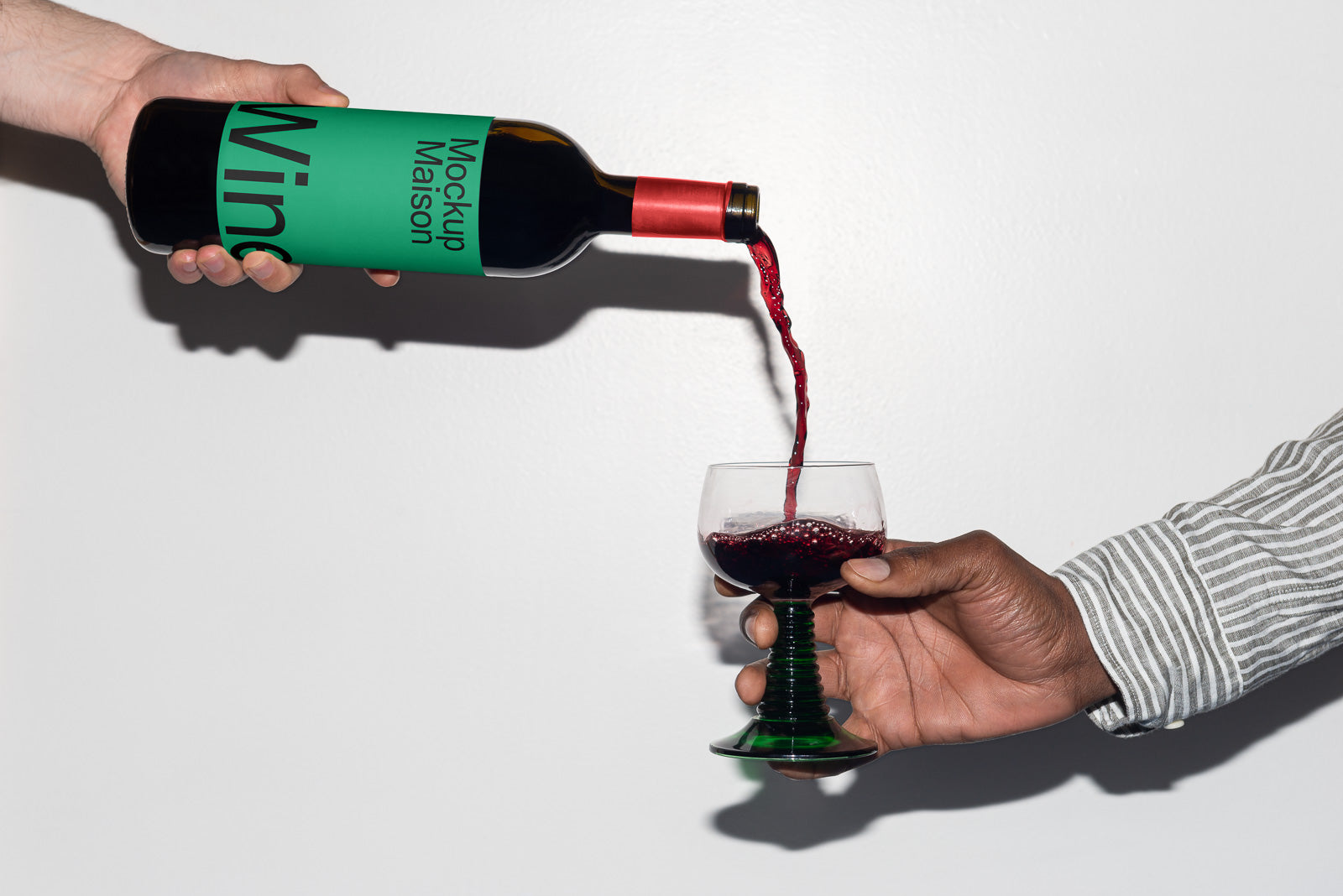 PSD mockup of a person pouring red wine from a bottle with a green label into a unique green-stemmed wine glass.