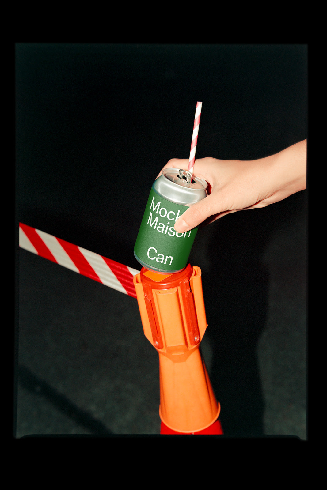 PSD mockup of a hand holding a green can with "Mock Maison Can" text, placed on an orange traffic cone with a red and white striped tape.
