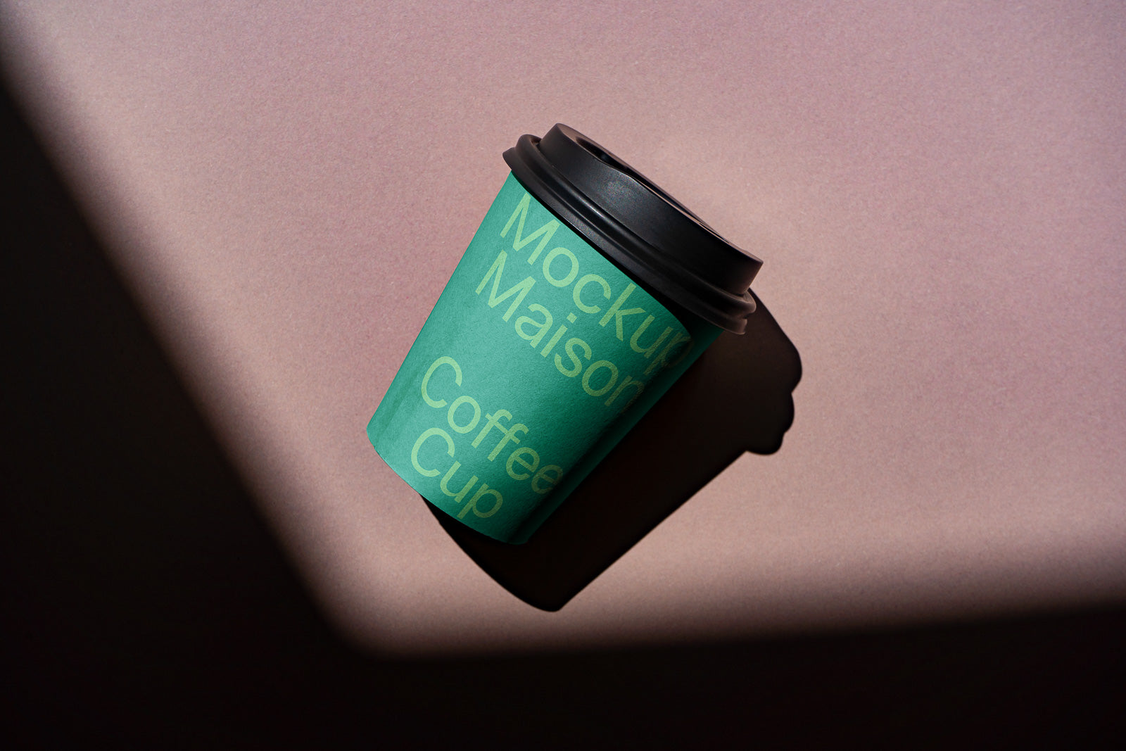 PSD mockup of a green coffee cup with a black lid casting a shadow on a pink surface, labeled with text for branding purposes.