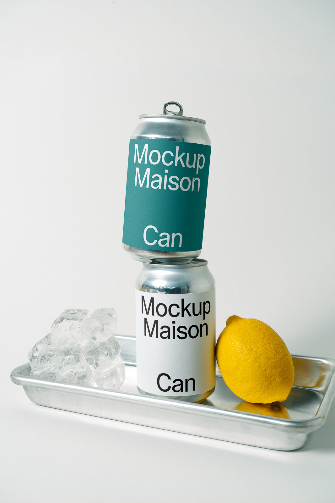 PSD mockup of two soda cans, one stacked on top of the other, labeled "Mockup Maison" with a lemon and ice cubes on a metal tray.