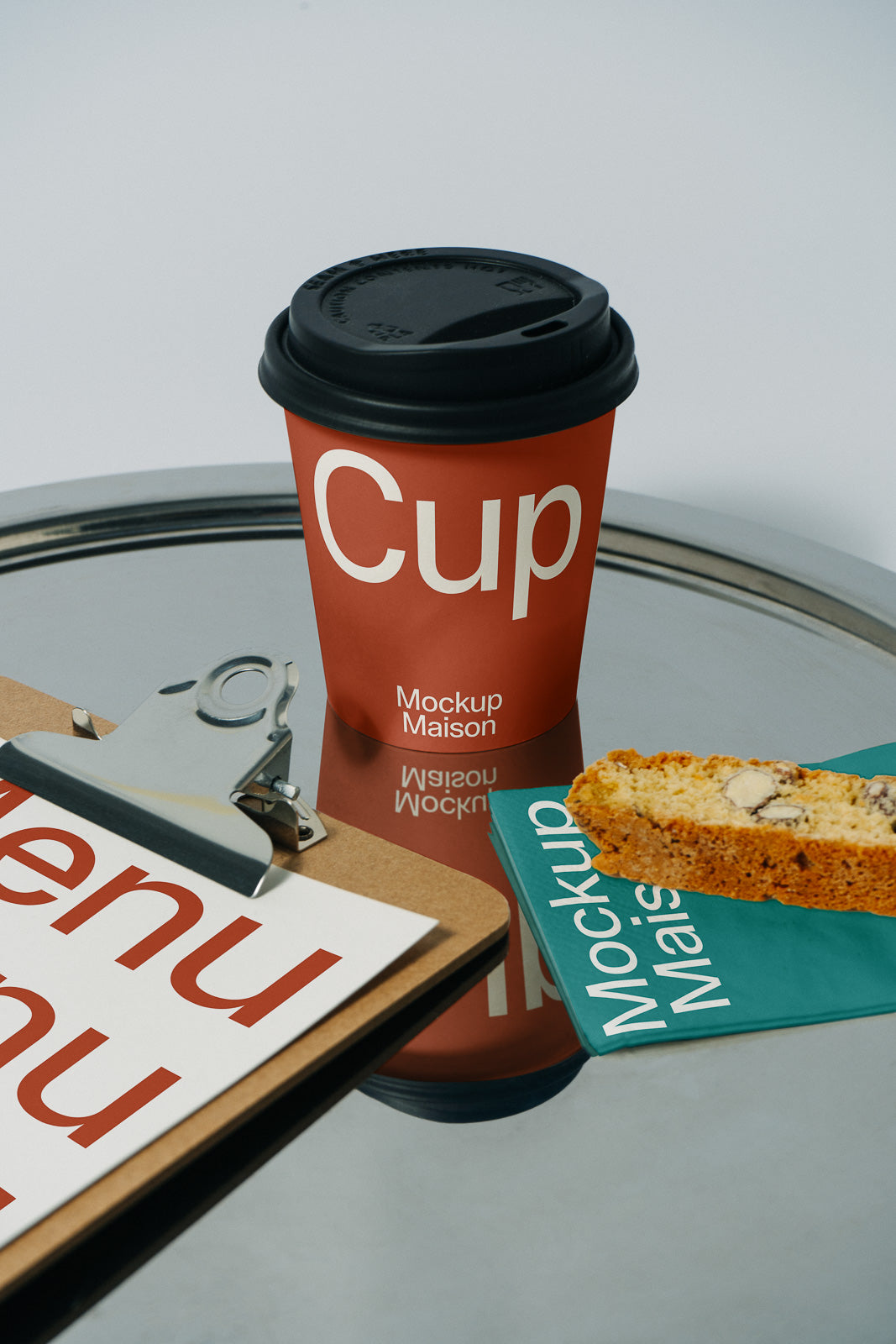 PSD mockup of a red takeaway cup with black lid, menu on clipboard, and biscotti on a branded napkin on a metallic surface.