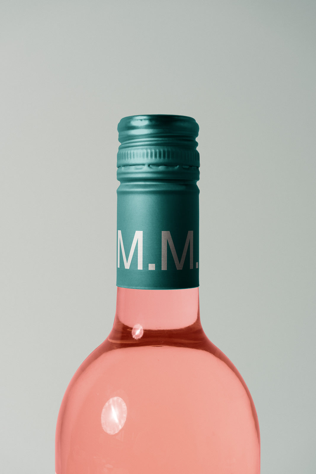 PSD mockup of a rose wine bottle with teal screw cap, featuring initials "M.M." on the cap, set against a neutral background.