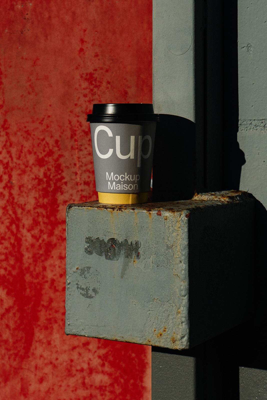 PSD mockup of a branded coffee cup with a gray wrap, placed on a weathered metal ledge, set against a textured red background.