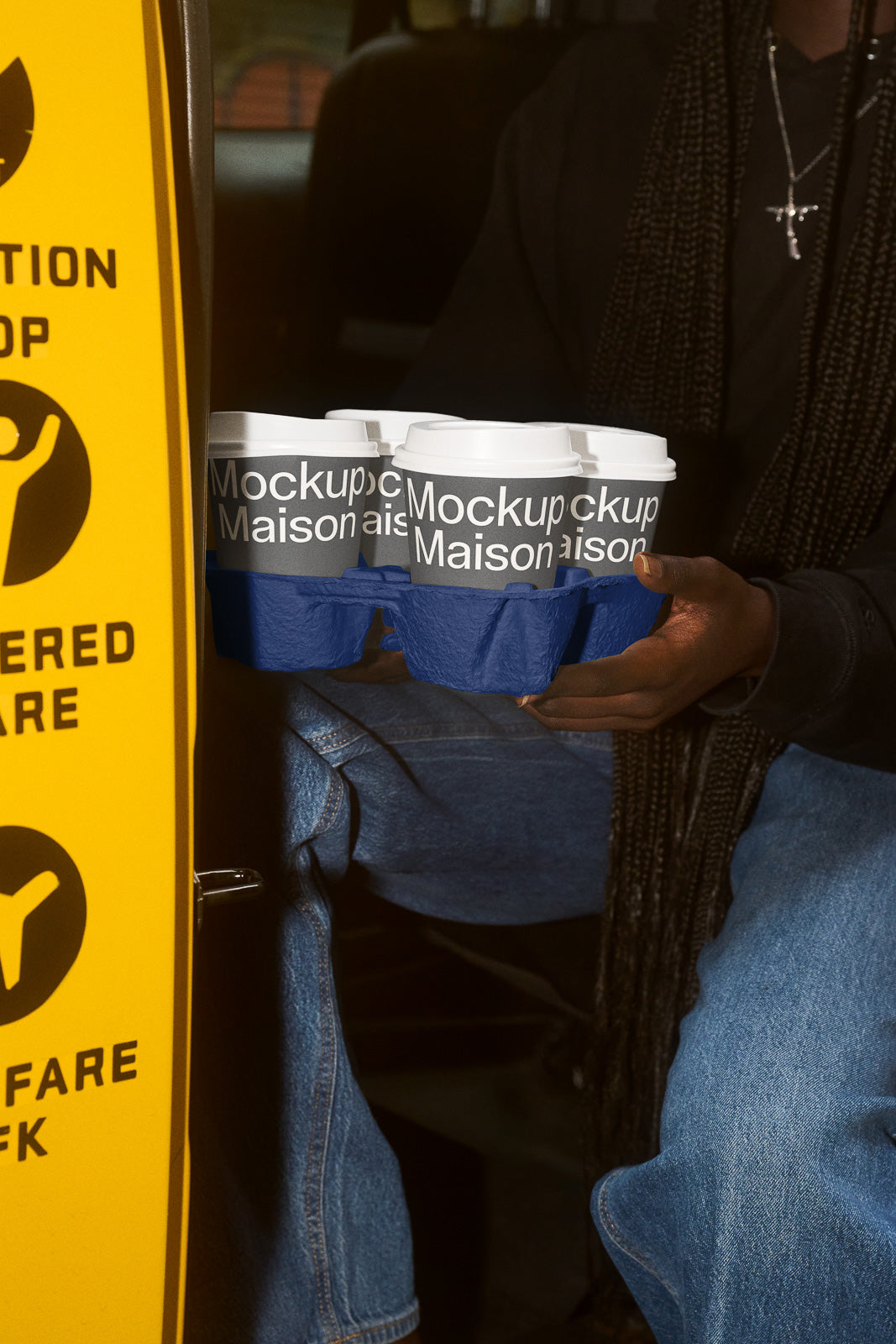PSD mockup of a hand holding a tray with four labeled coffee cups inside a vehicle, next to a yellow door signage.