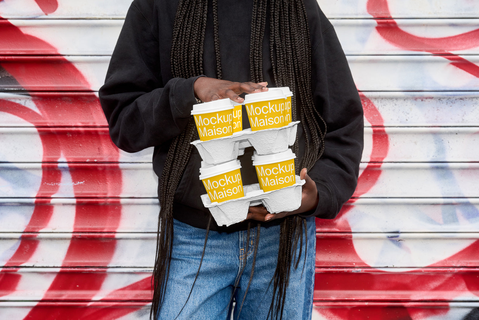 PSD mockup of a person holding two coffee cup holders with cups that have "Mockup Maison" branding, standing against a colorful graffiti background.