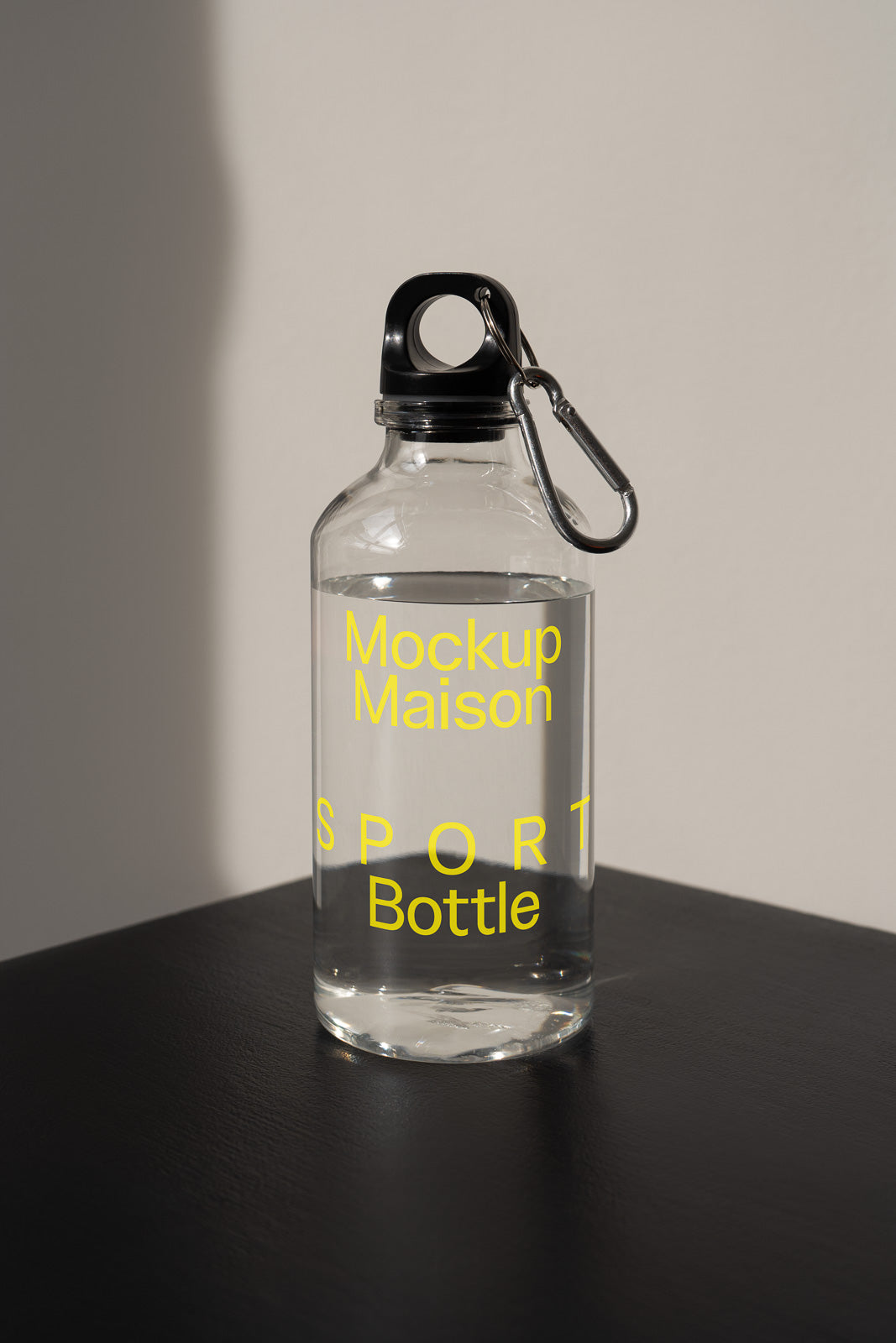 PSD mockup of a clear plastic sport bottle with a black cap and carabiner, featuring yellow text reading "Mockup Maison SPORT Bottle" against a neutral background.