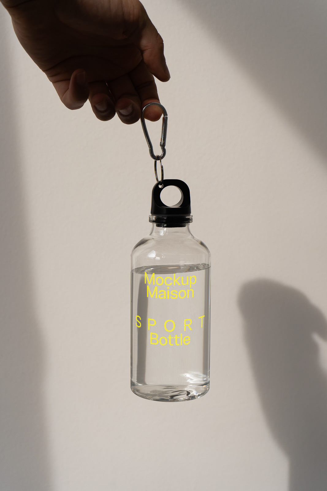 PSD mockup of a transparent sport bottle with a carabiner clip, held by a hand, casting a shadow on a light background.