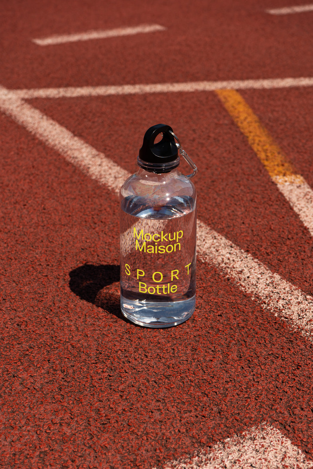 PSD mockup of a clear sport bottle on a running track, with yellow text reading "Mockup Maison SPORT Bottle."