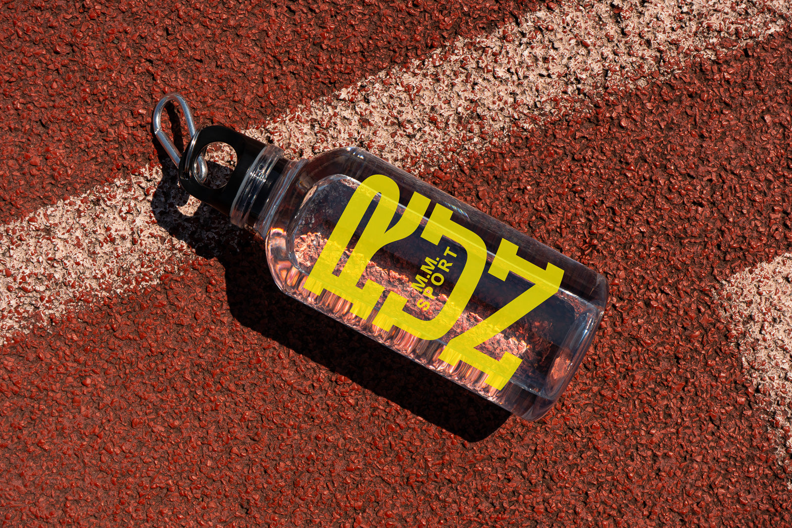 PSD mockup of a clear sports bottle with bold yellow text on a textured red running track with white lines.