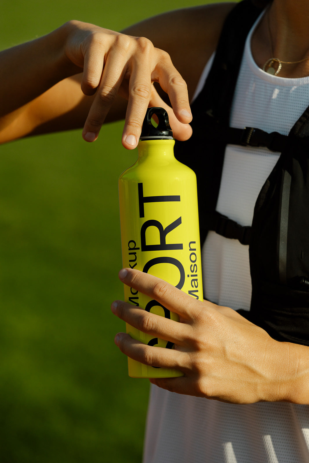 PSD mockup of a person holding a bright yellow sports bottle with bold black text, set against a blurred green background.