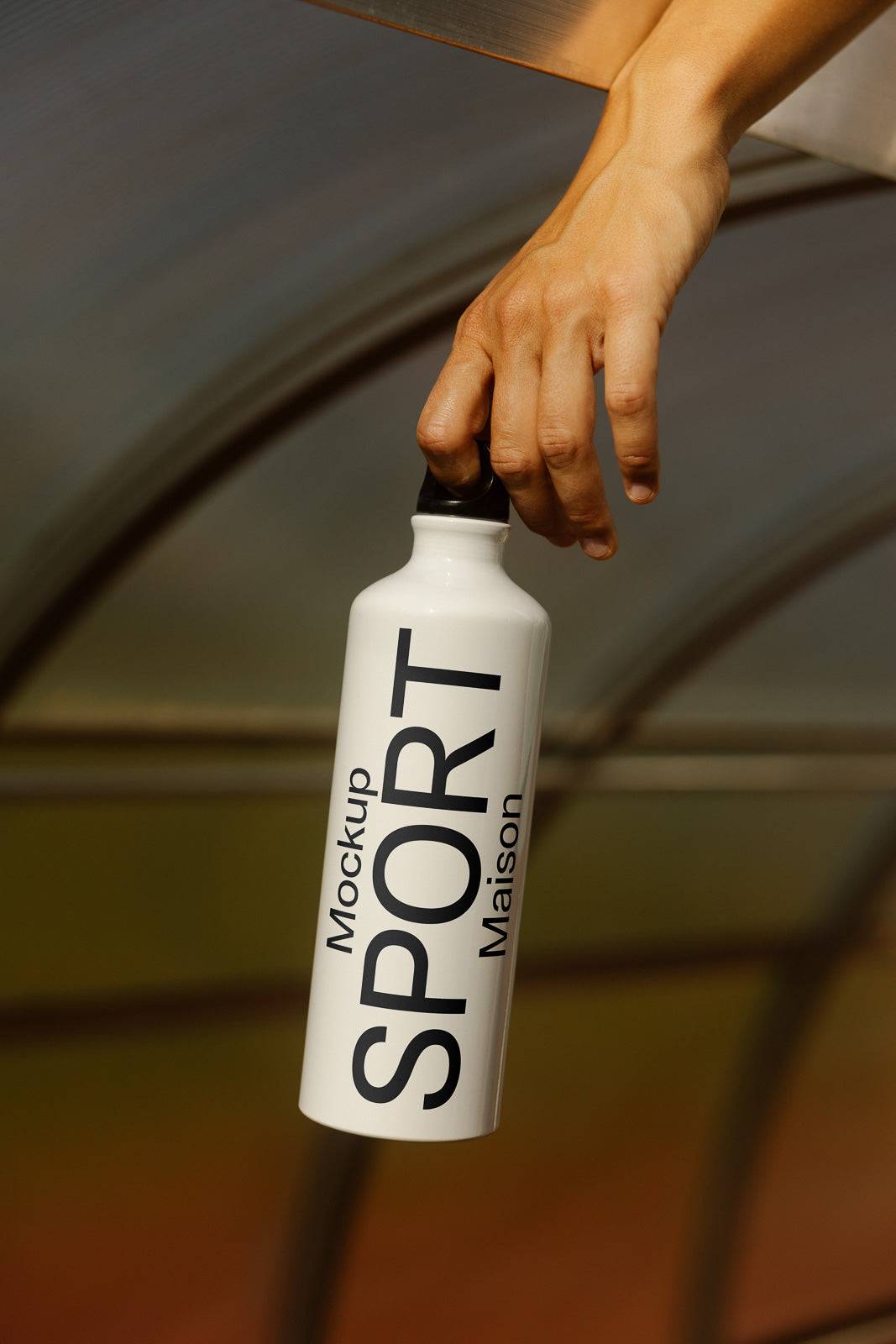 PSD mockup of a white sports bottle labeled "Mockup Maison SPORT," held by a hand against a blurred curved background, emphasizing sleek design.