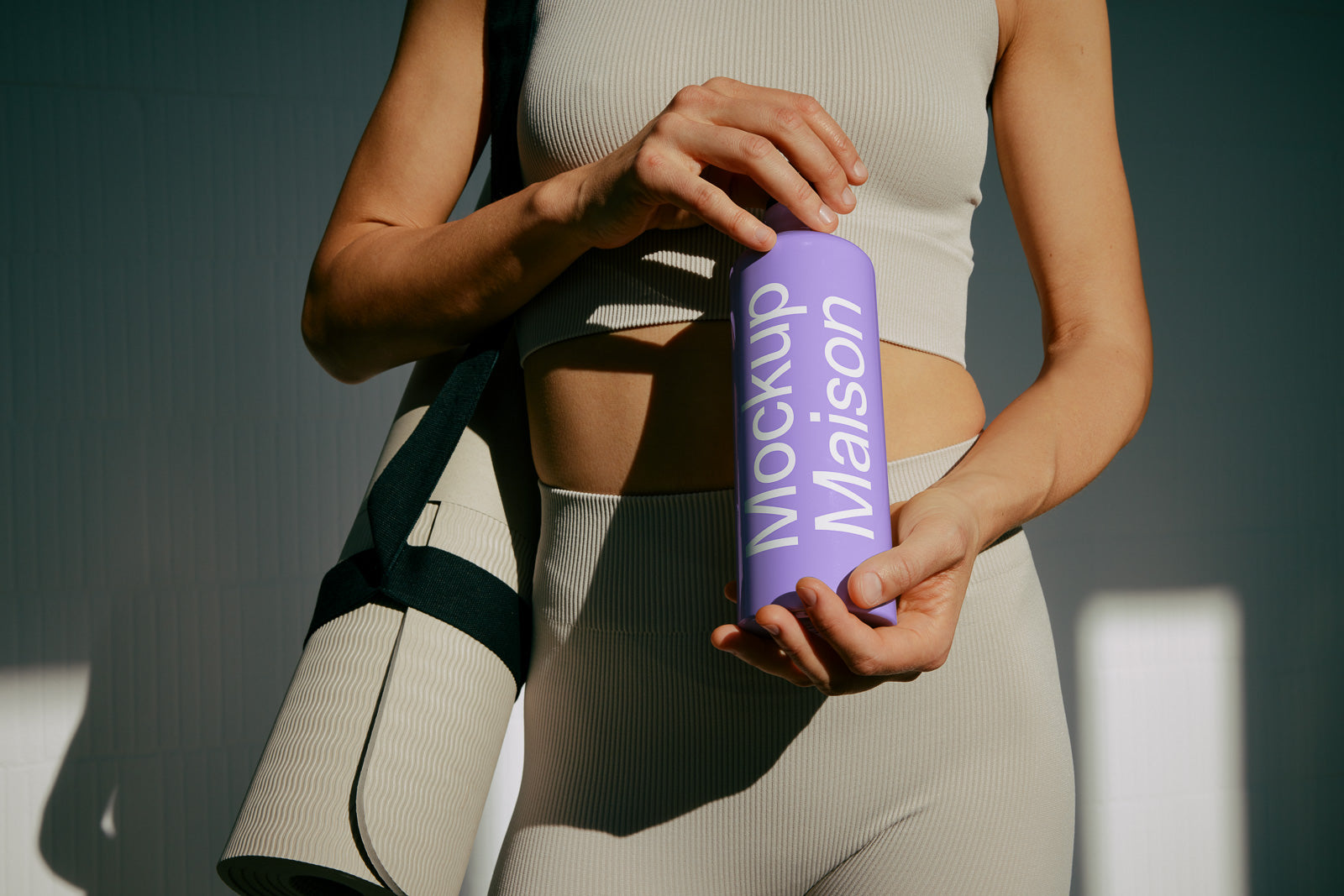 PSD mockup of a person holding a purple water bottle with "Mockup Maison" text, wearing a beige athletic outfit, and carrying a rolled yoga mat.
