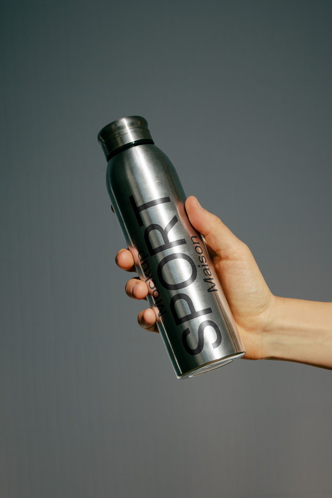 PSD mockup of a stainless steel sport water bottle held in a hand against a plain background, showcasing sleek design and typography.