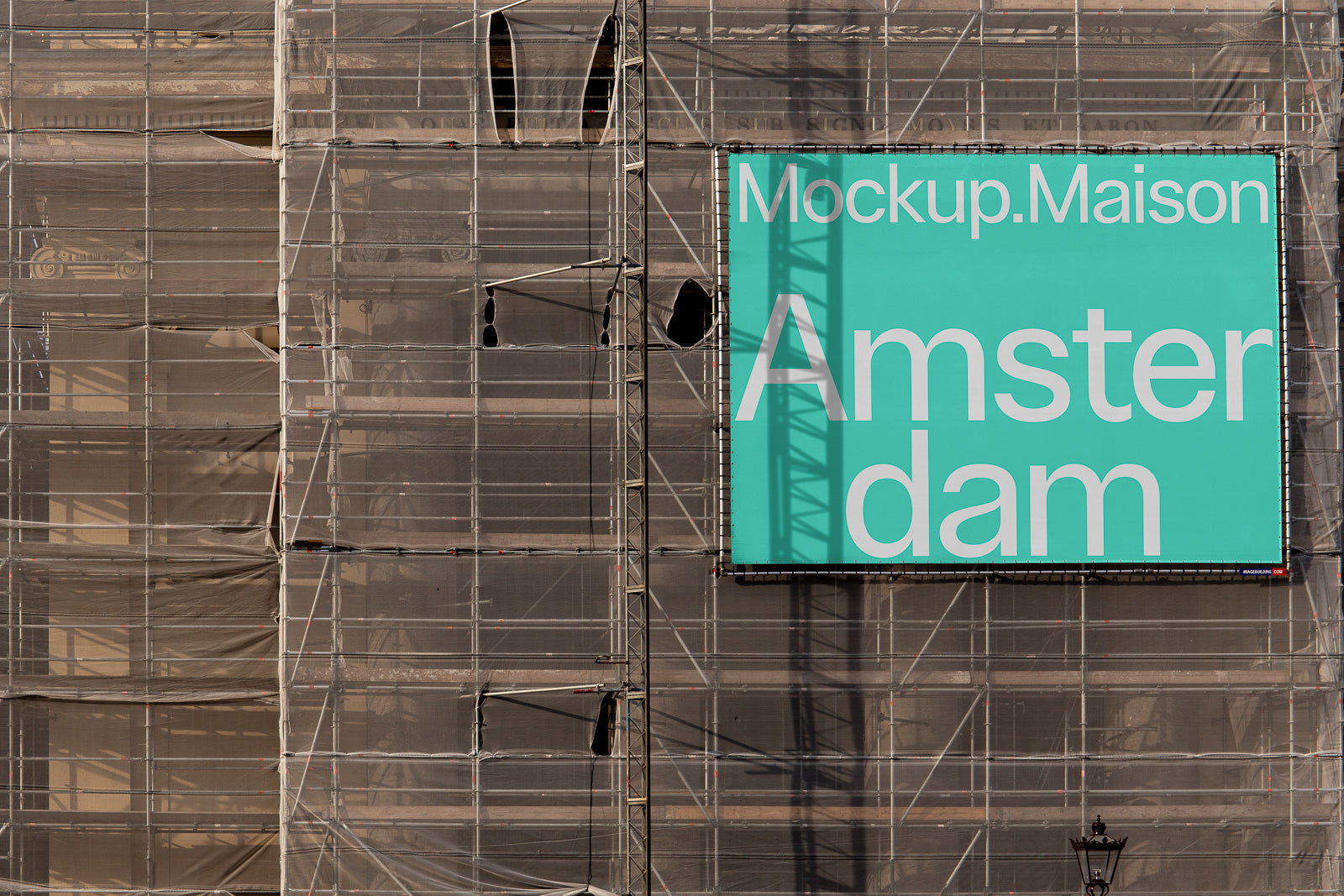 PSD mockup of a large teal billboard with white text reading "Mockup.Maison Amsterdam," displayed on a building under construction with scaffolding.