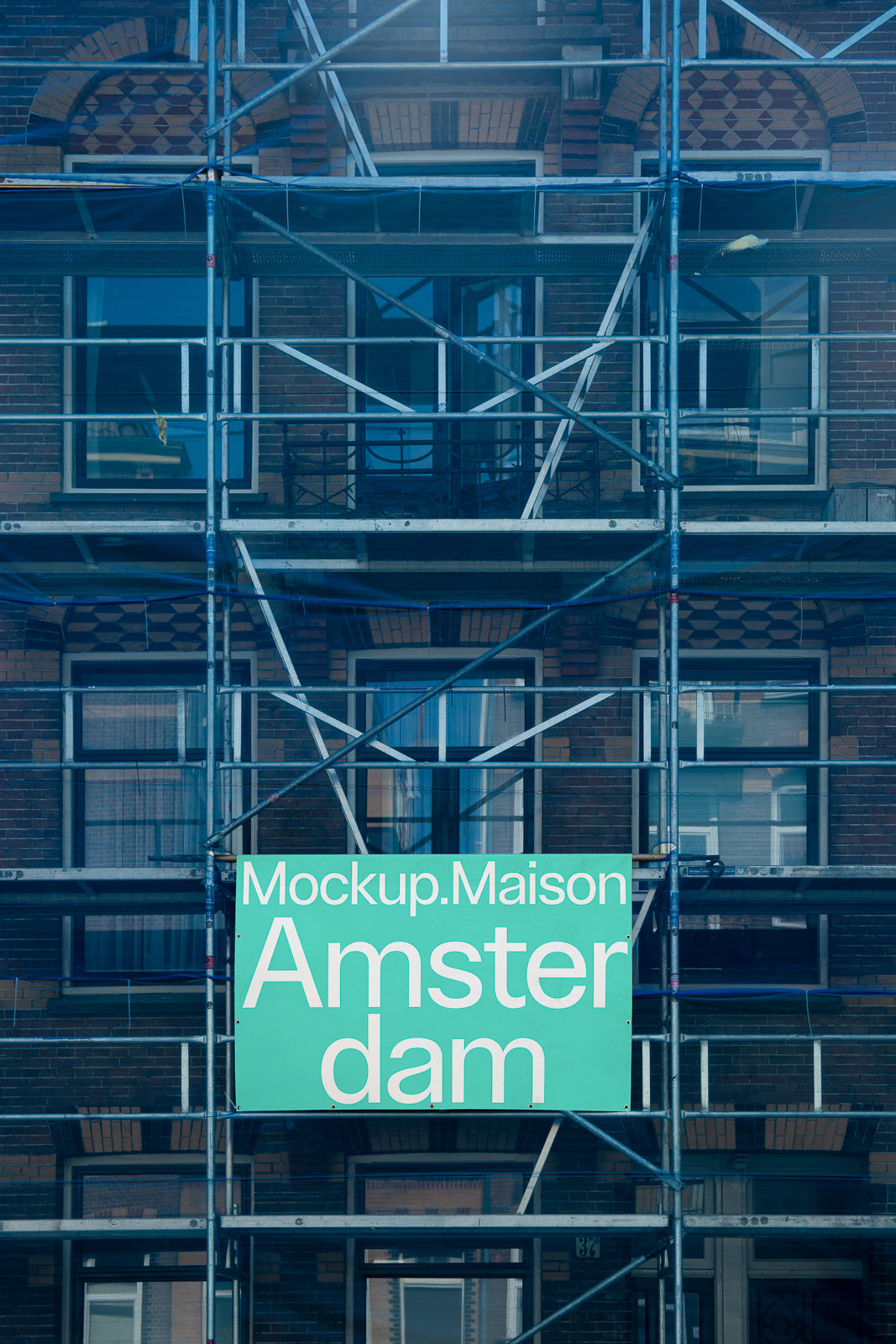 PSD mockup of a building facade with scaffolding and a teal sign displaying "Mockup.Maison Amsterdam" in large white text.