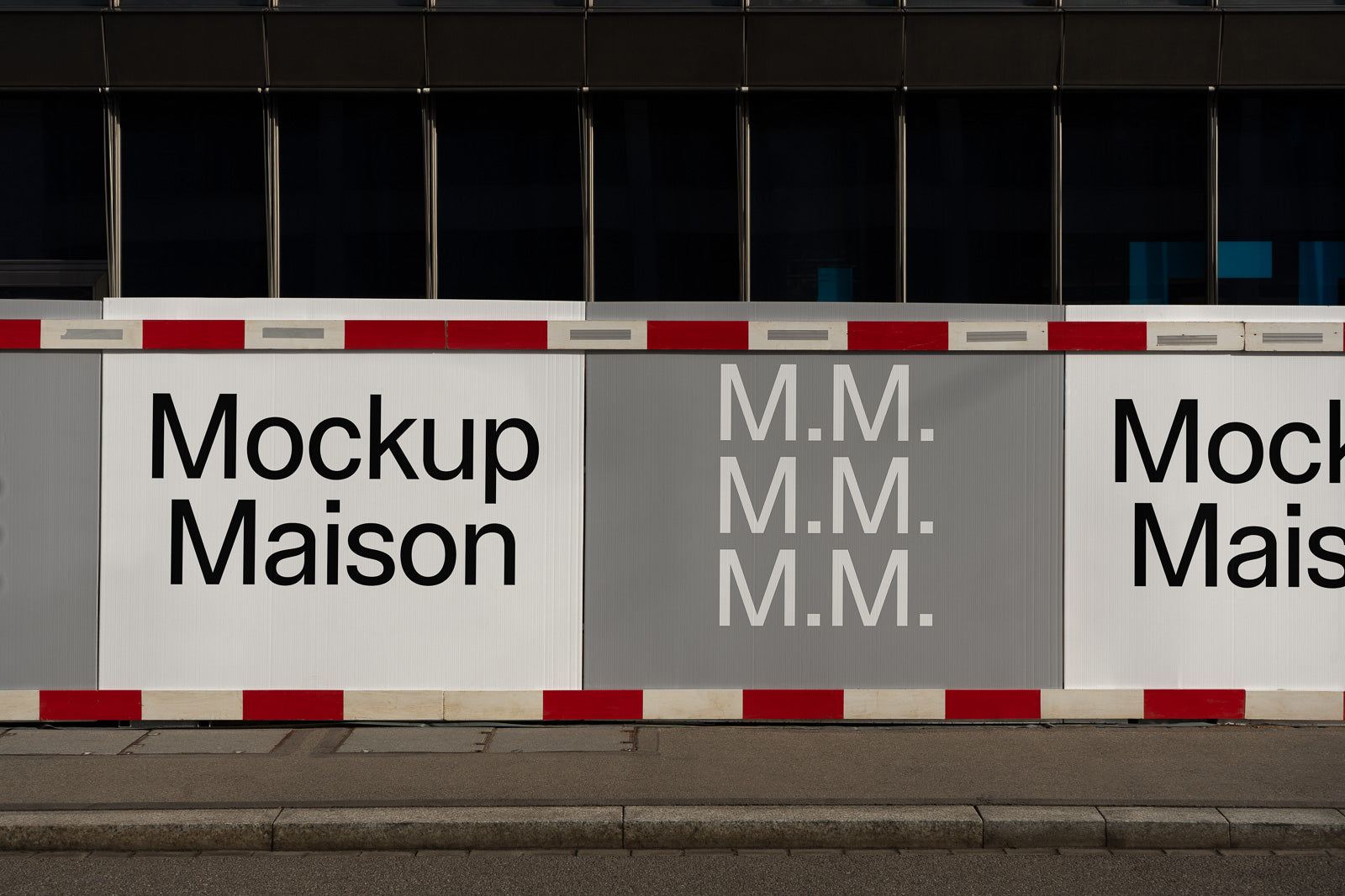 PSD mockup of construction hoarding featuring bold text "Mockup Maison" and "M.M." on alternating panels against a modern building backdrop.