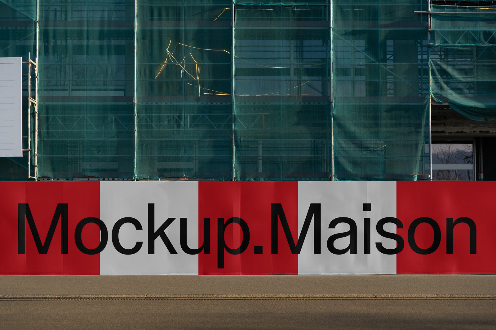 PSD mockup of a construction site barrier displaying bold text "Mockup.Maison" in black on a red and white background, set against a green netted building.